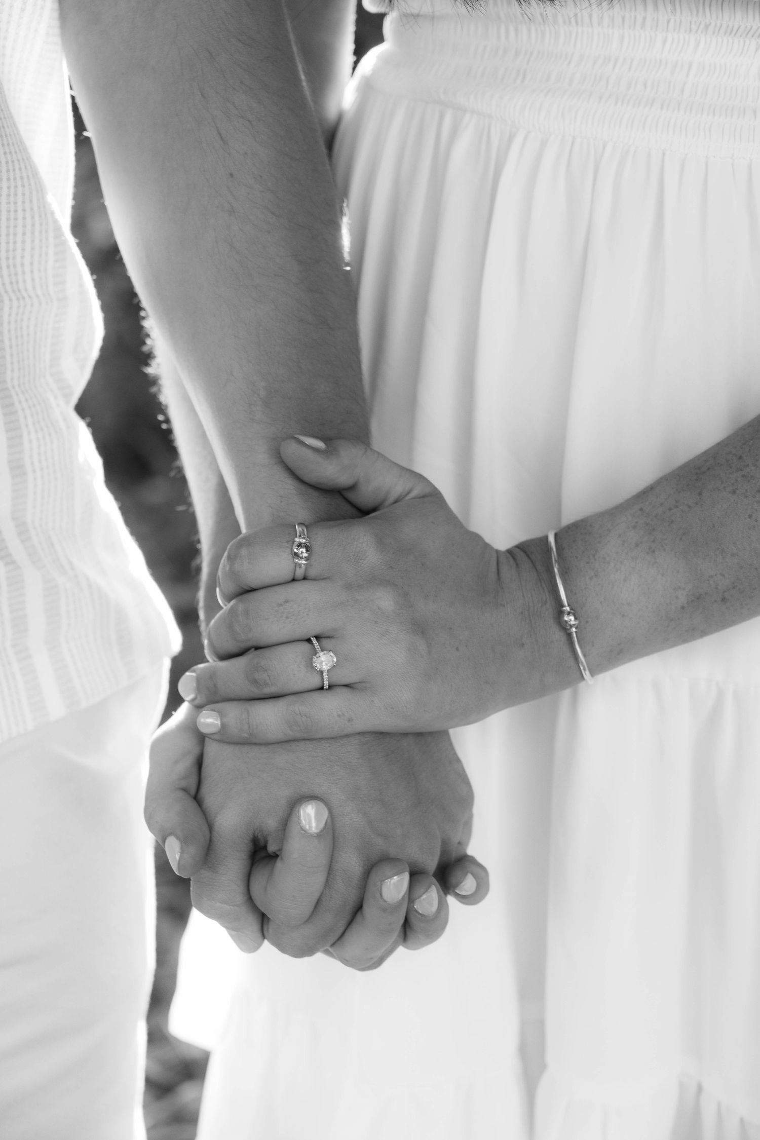 Black and white close-up of couple holding hands showing engagement ring and bracelet.