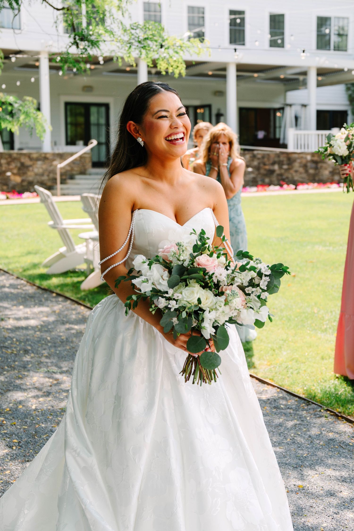 Joyful bride laughing while holding white and blush bouquet during outdoor summer wedding ceremony.