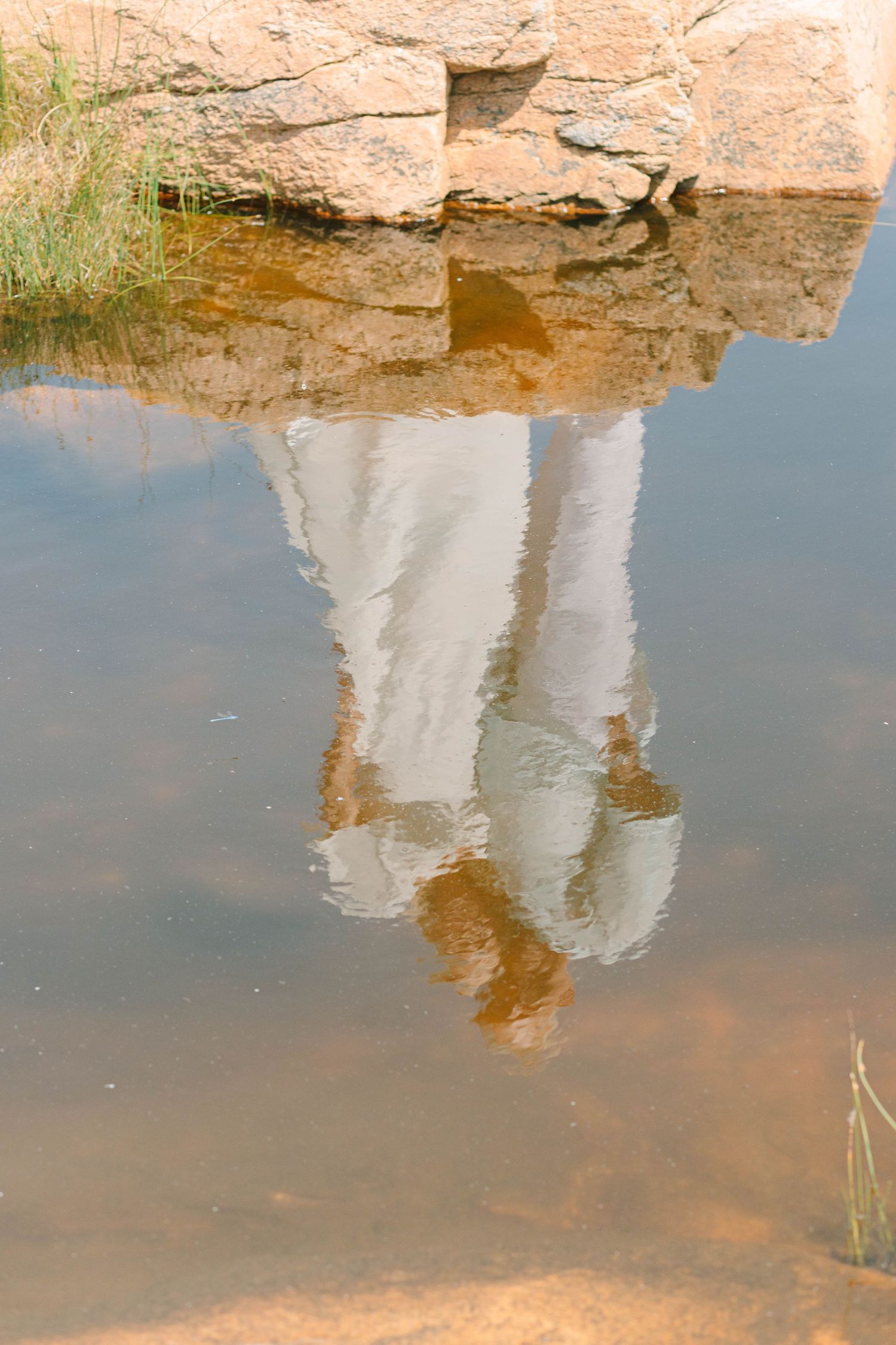 Reflection of couple in white wedding attire mirrored in a rocky tidal pool on the coast.