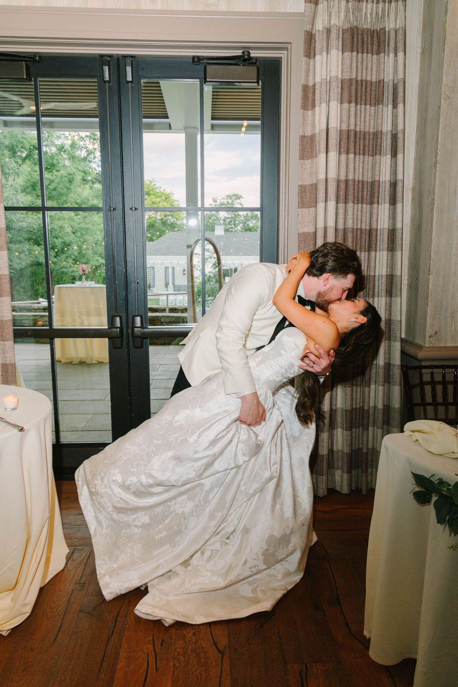 Groom dips bride in romantic kiss after cake cutting at elegant wedding reception.