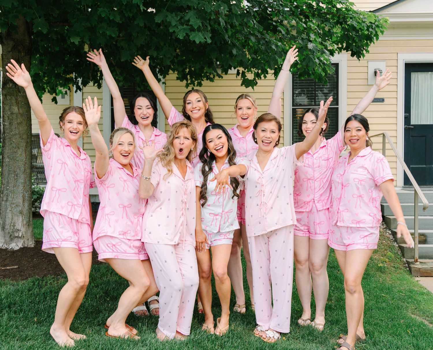 Bride and bridesmaids celebrating in matching pink pajamas on green lawn.