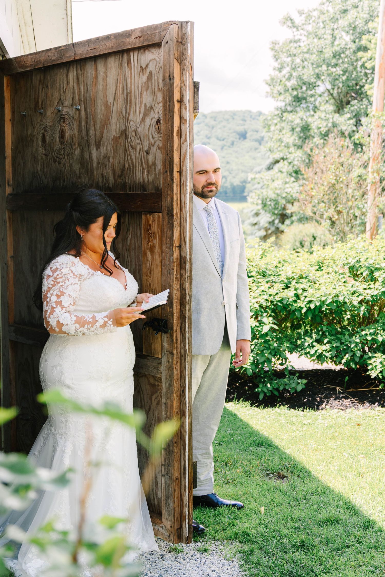 Bride reading vows privately to groom around wooden barn door outside.