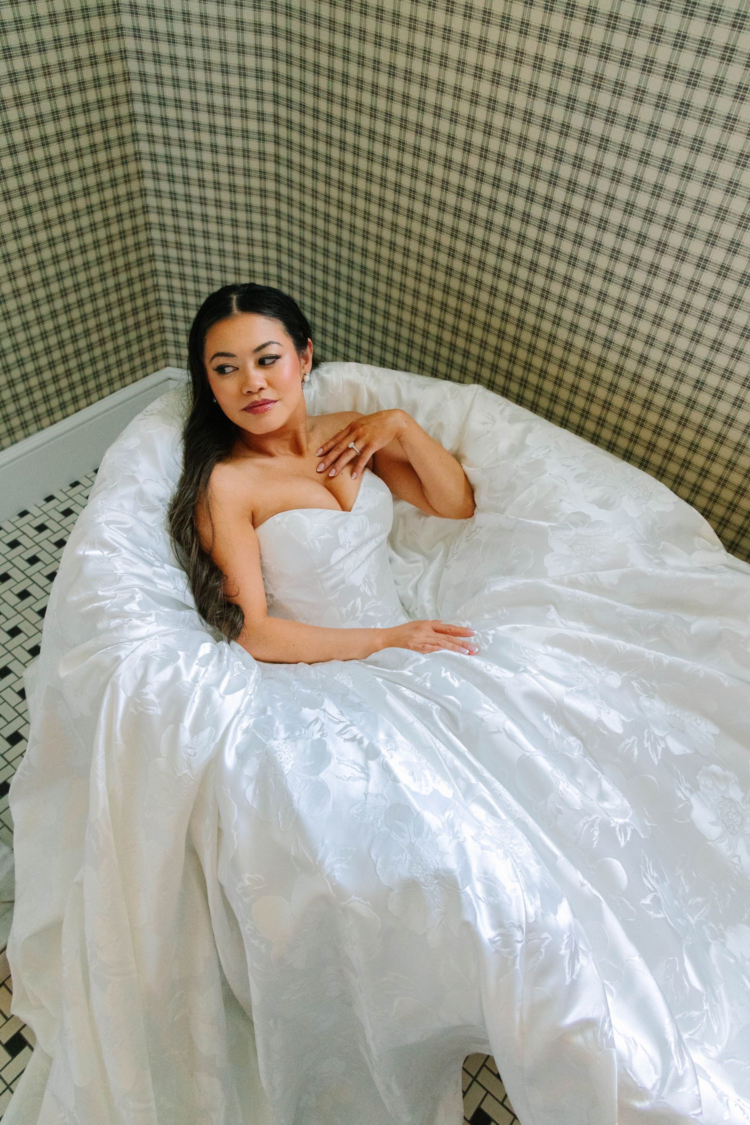 Beautiful bride in a white strapless ballgown reclines in a bathtub, posing for bridal portraits.