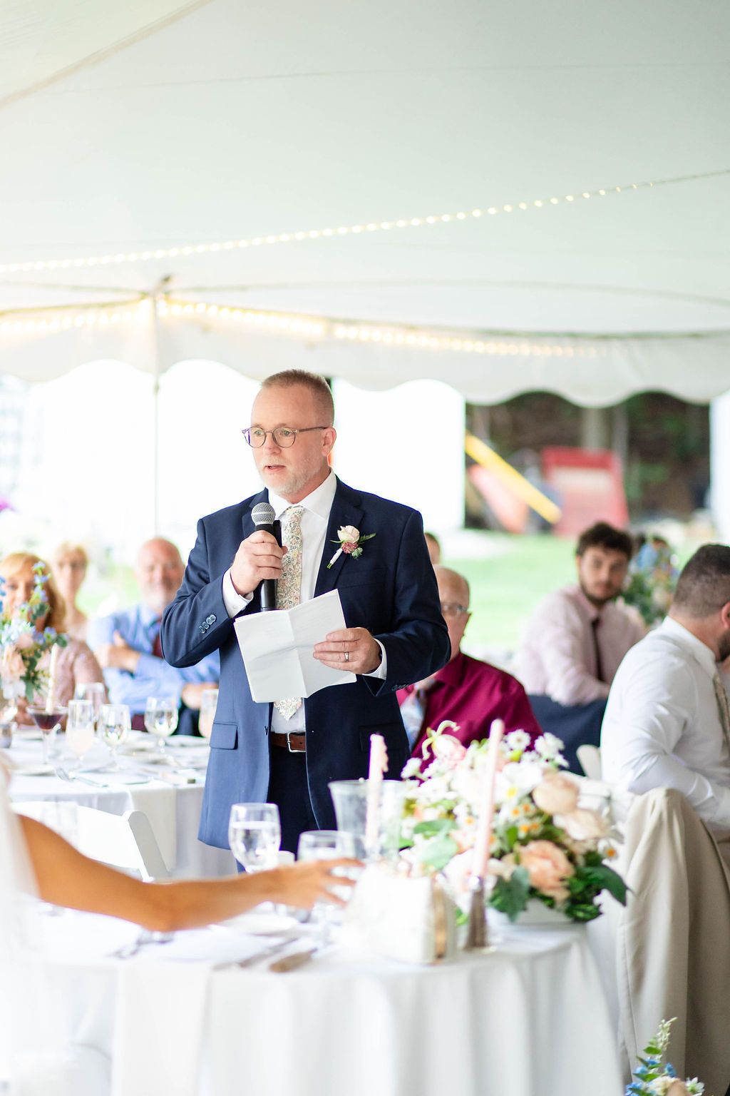 Father of the bride delivers heartfelt speech at outdoor tented wedding reception.