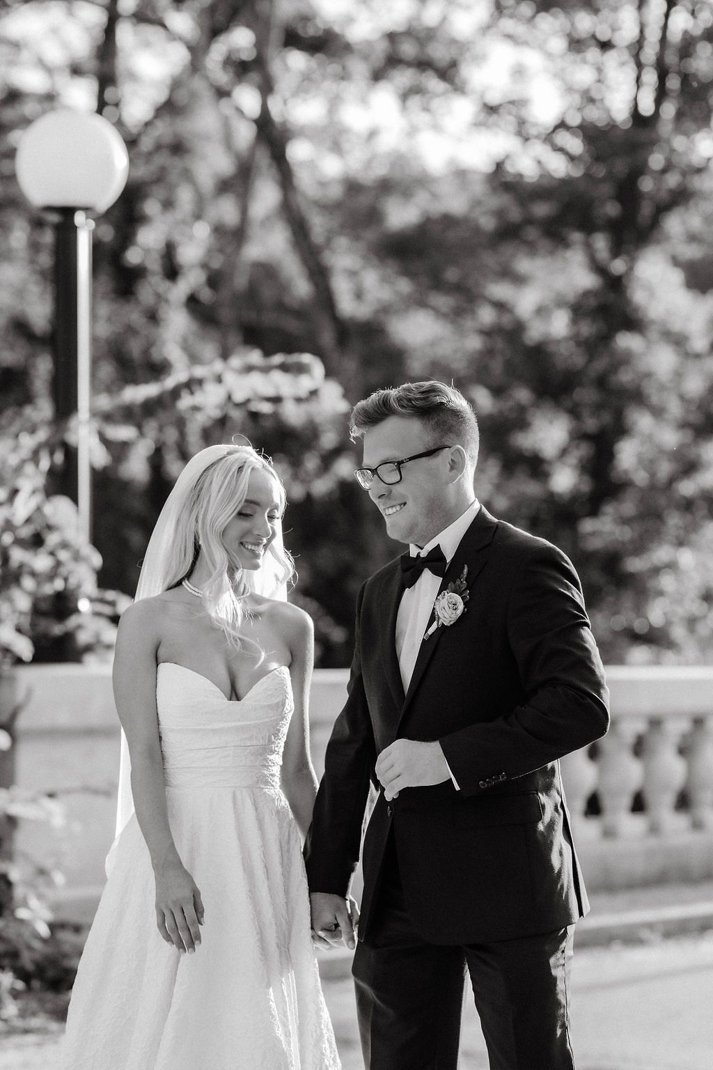 Black and white photo of smiling bride and groom walking together outdoors on their wedding day.