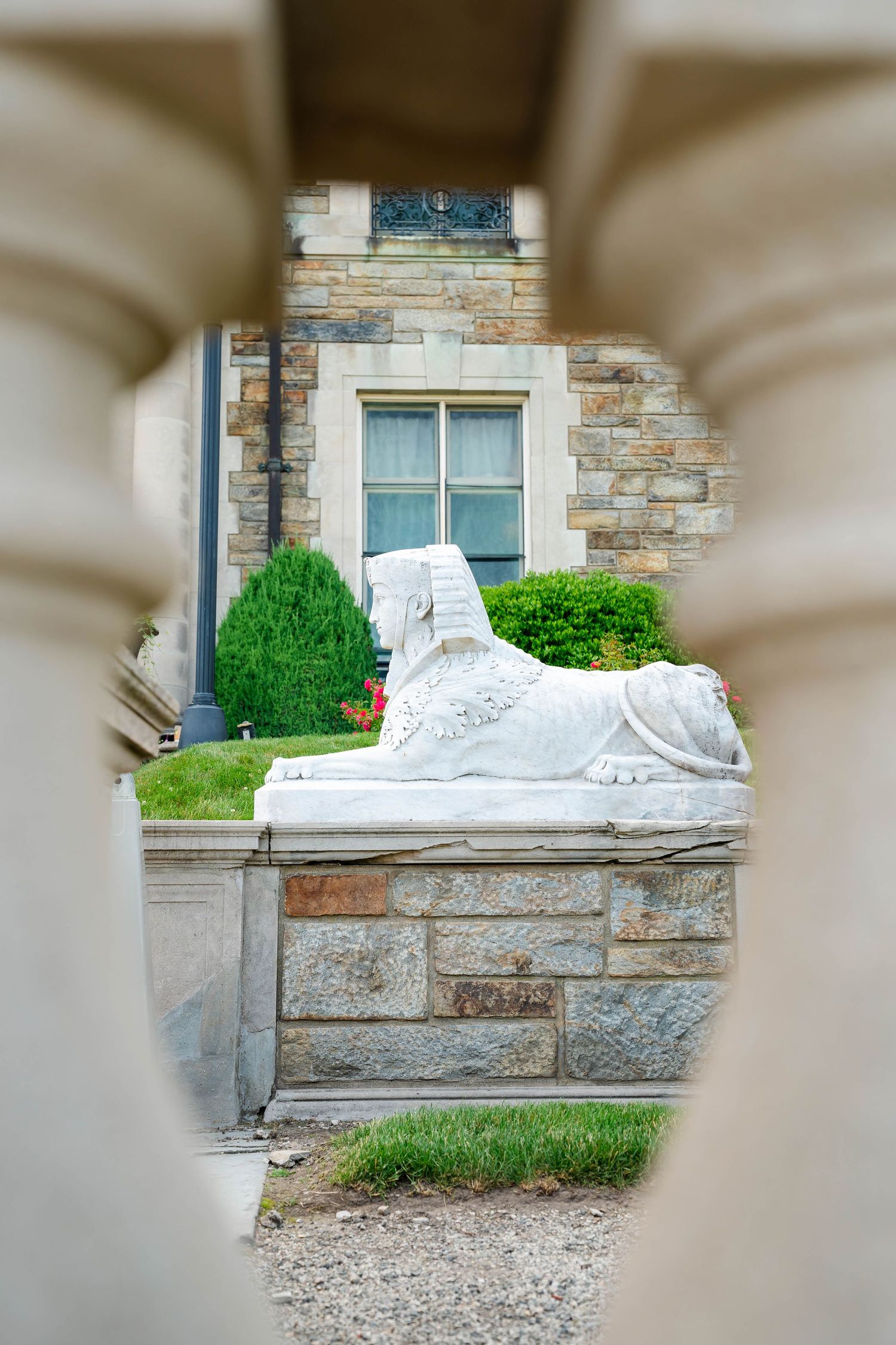 White marble sphinx statue viewed through stone columns outside a historic limestone building.