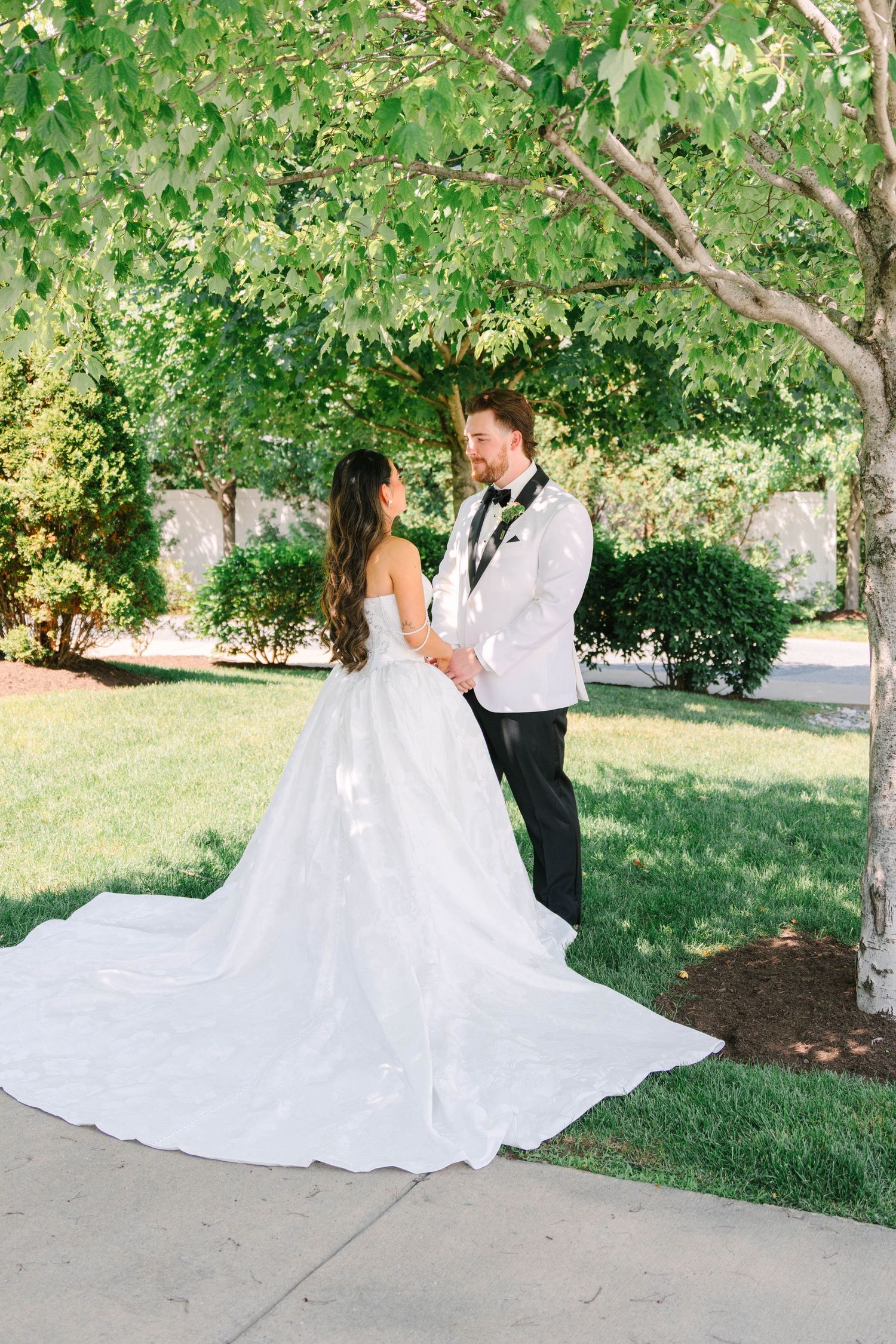 Bride and groom gazing at each other holding hands under a tree at outdoor summer wedding.