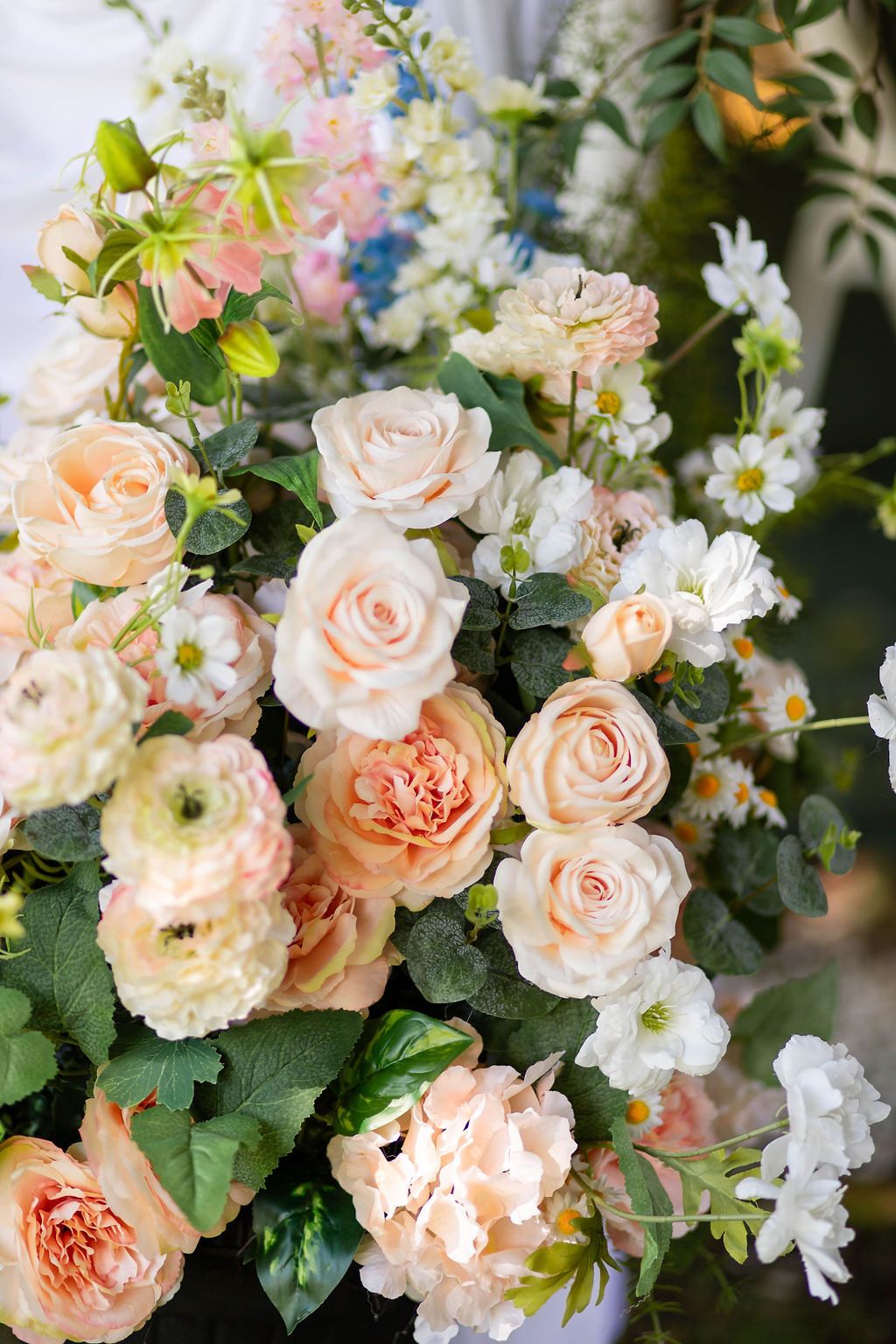 Lush wedding floral arrangement featuring peach garden roses, ranunculus, daisies, and white blooms.