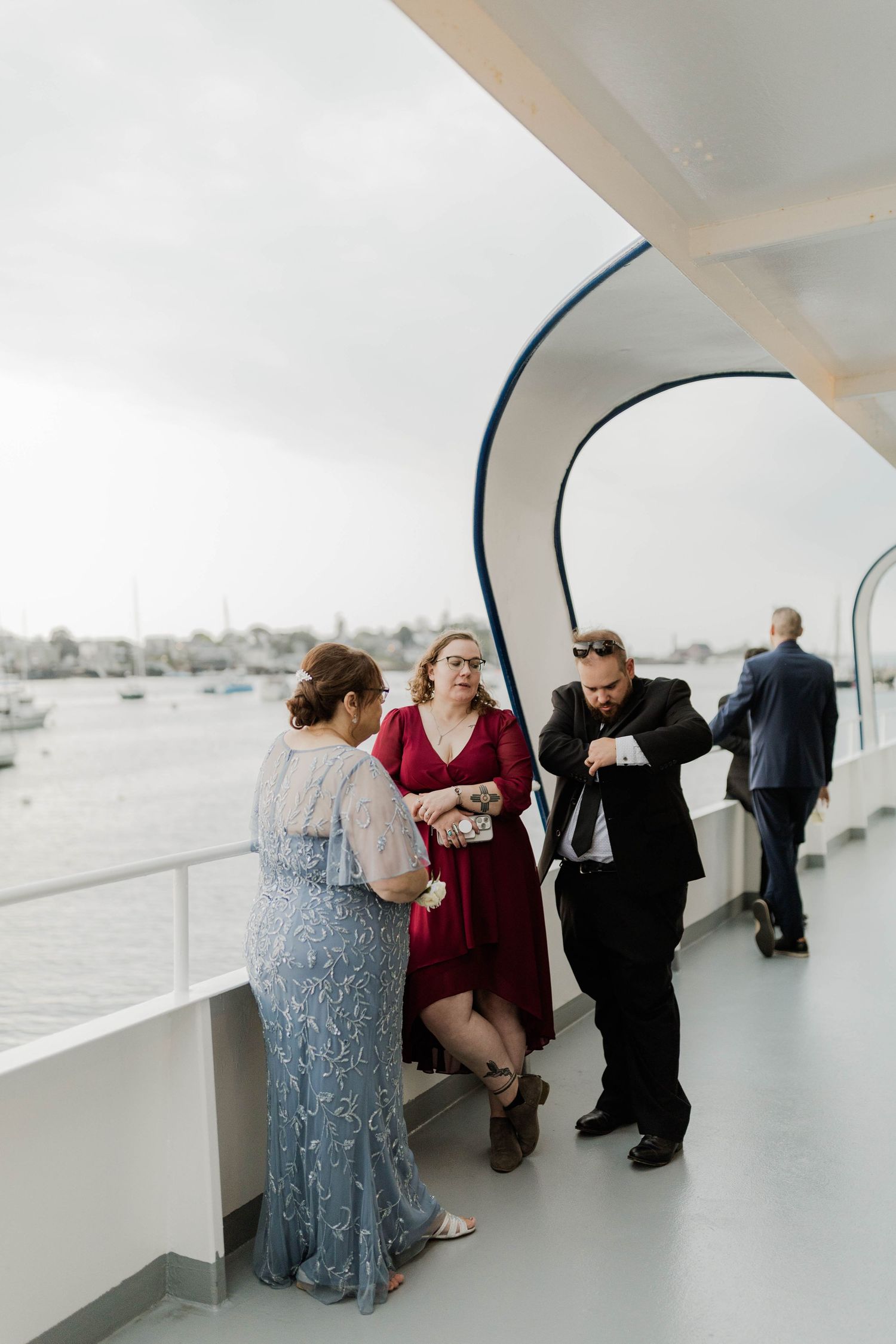 Wedding guests socializing on boat deck overlooking harbor during reception.