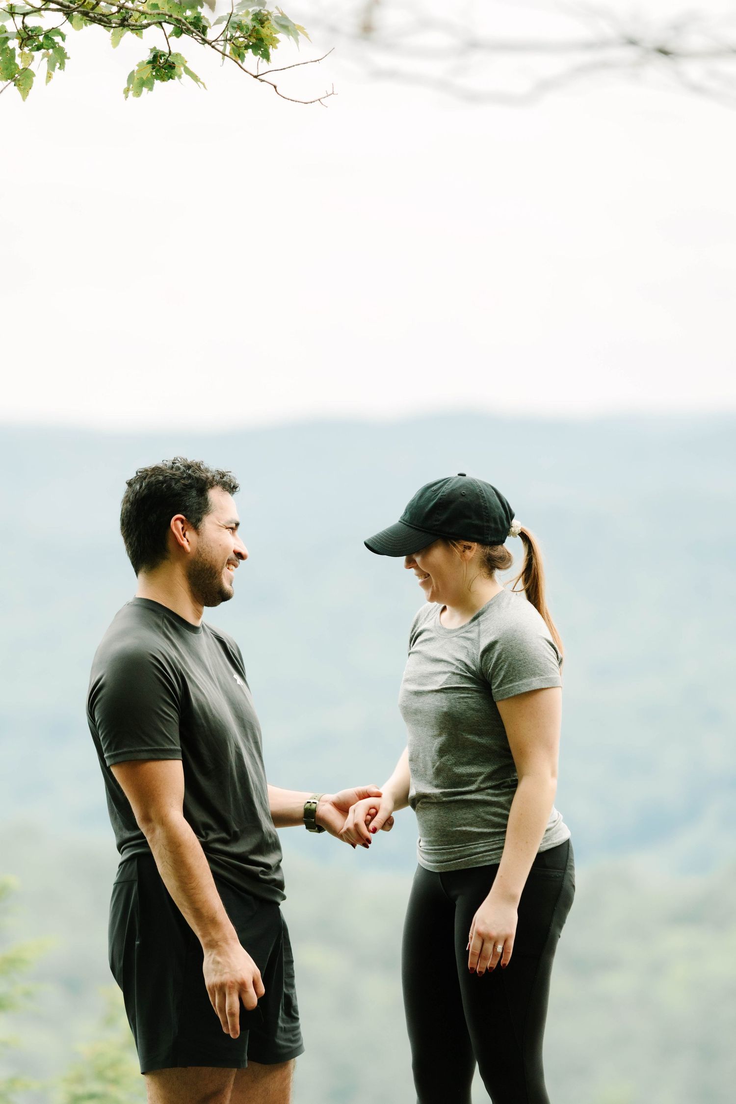 Happy couple holding hands and smiling at each other on a rocky overlook with mountain views.