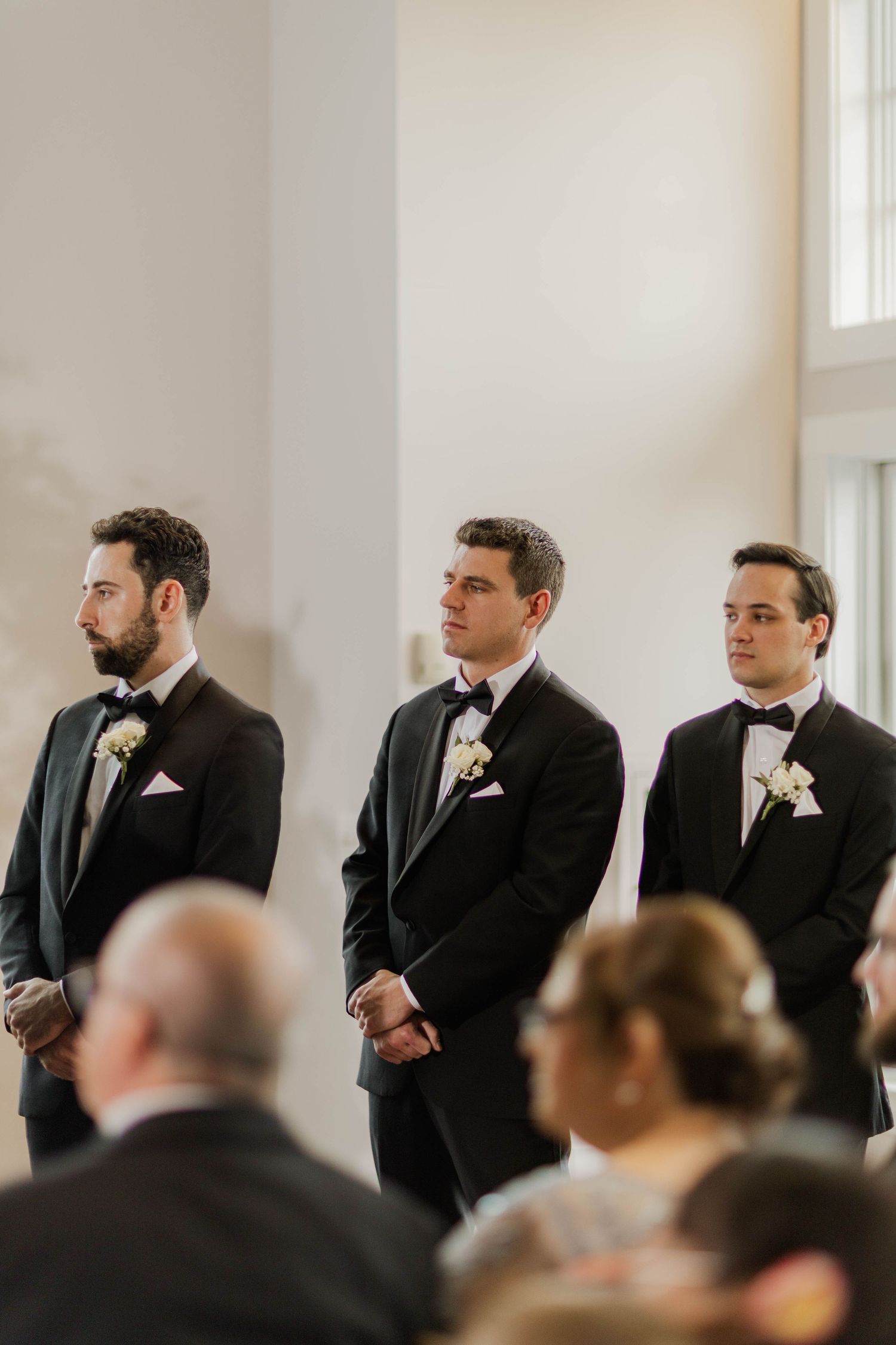 Three groomsmen in black tuxedos standing at the altar during a wedding ceremony.