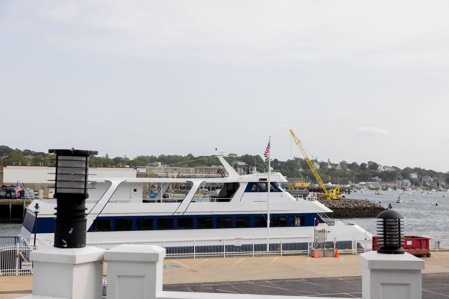 White passenger ferry docked at a harbor pier with calm waters and a cloudy sky in the background.