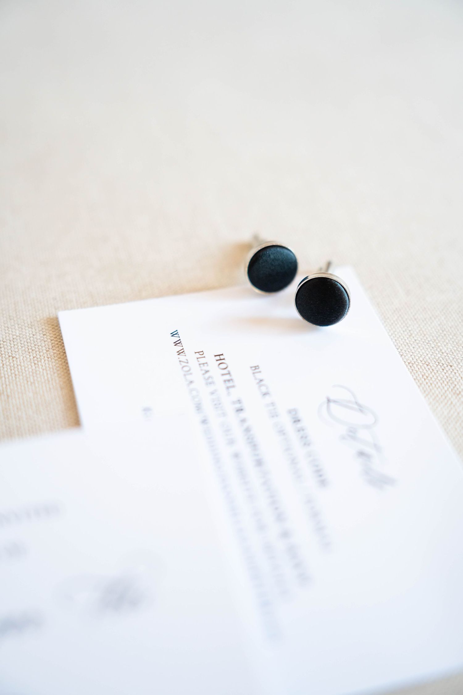 Black round cufflinks resting on a white hotel card on a linen surface.