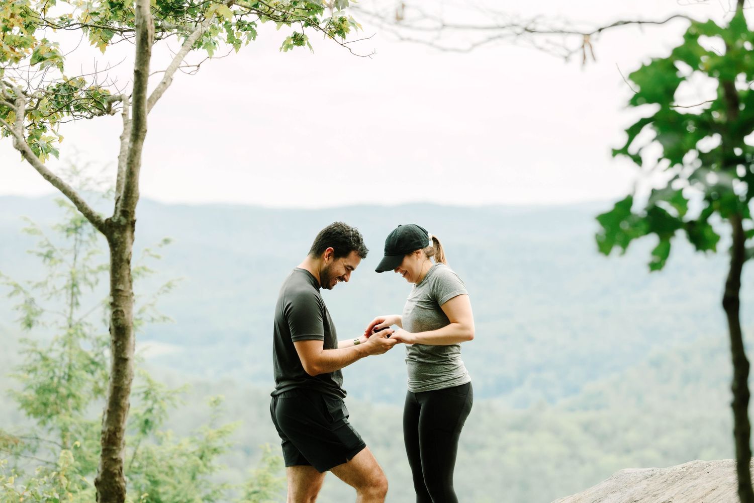 Couple sharing a moment on a mountain overlook surrounded by lush green trees during a hiking trip.