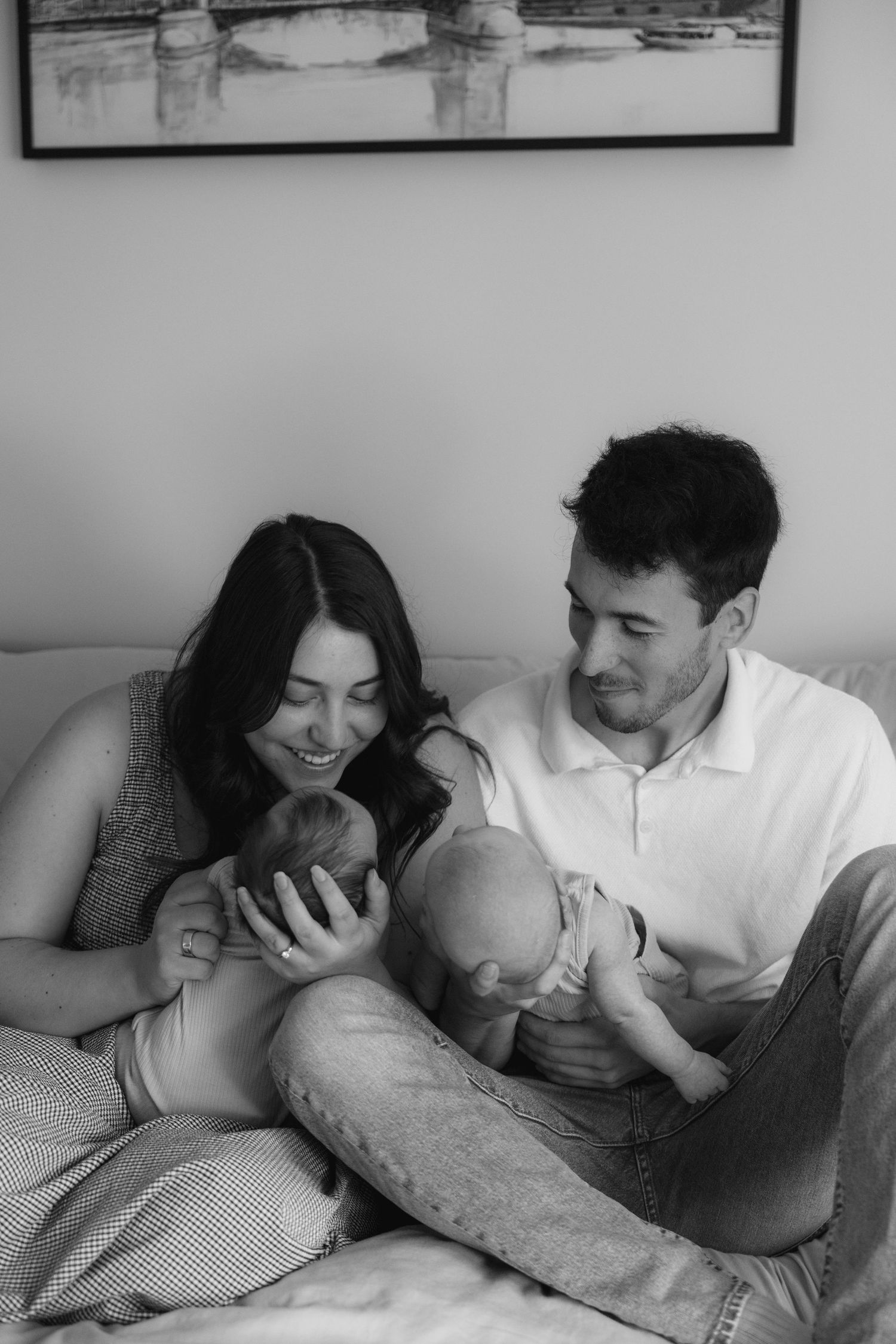 Black and white photo of parents on a bed lovingly holding their twin newborn babies.