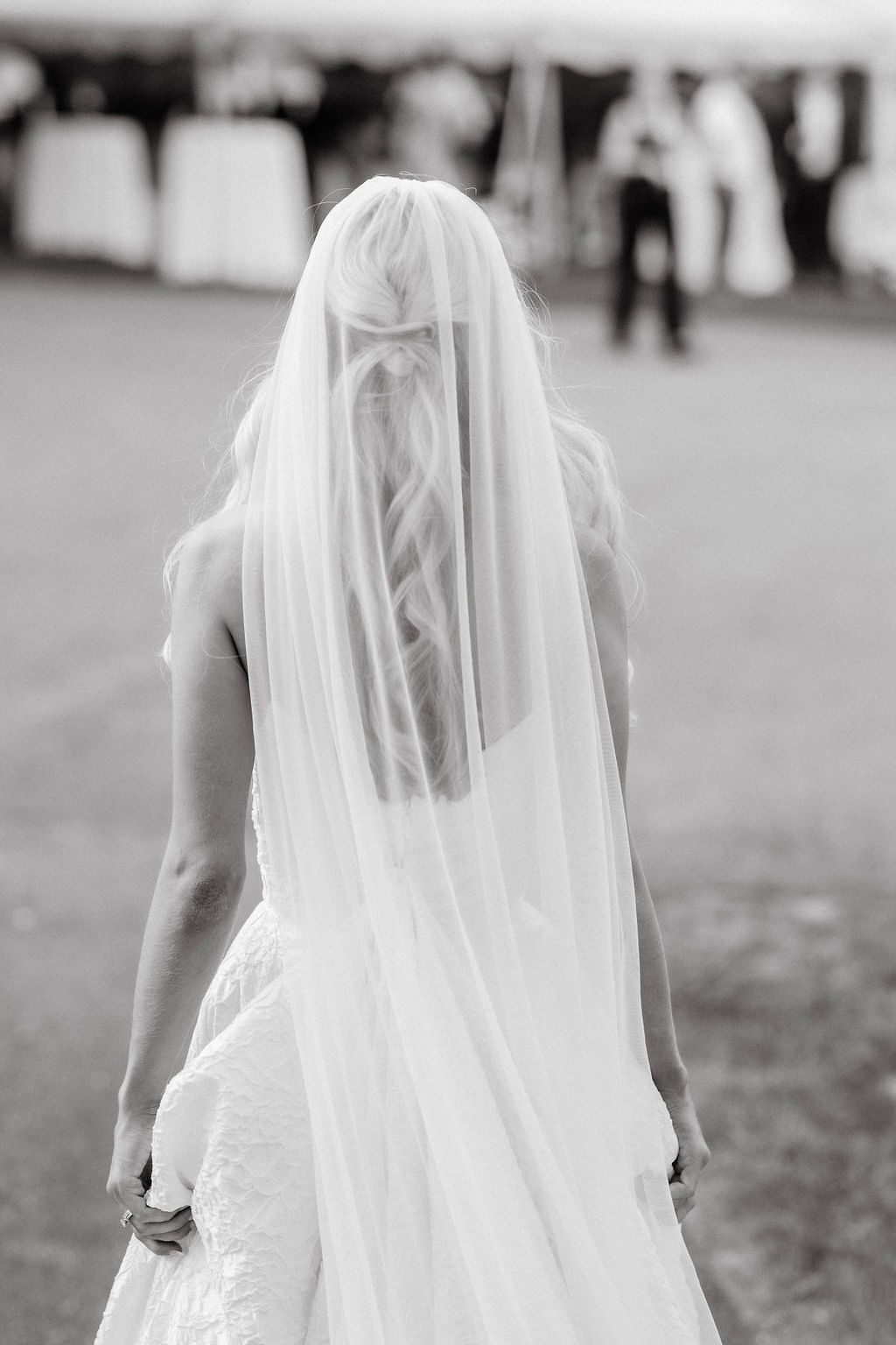 Black and white photo of bride walking away wearing long veil with braided hair detail.