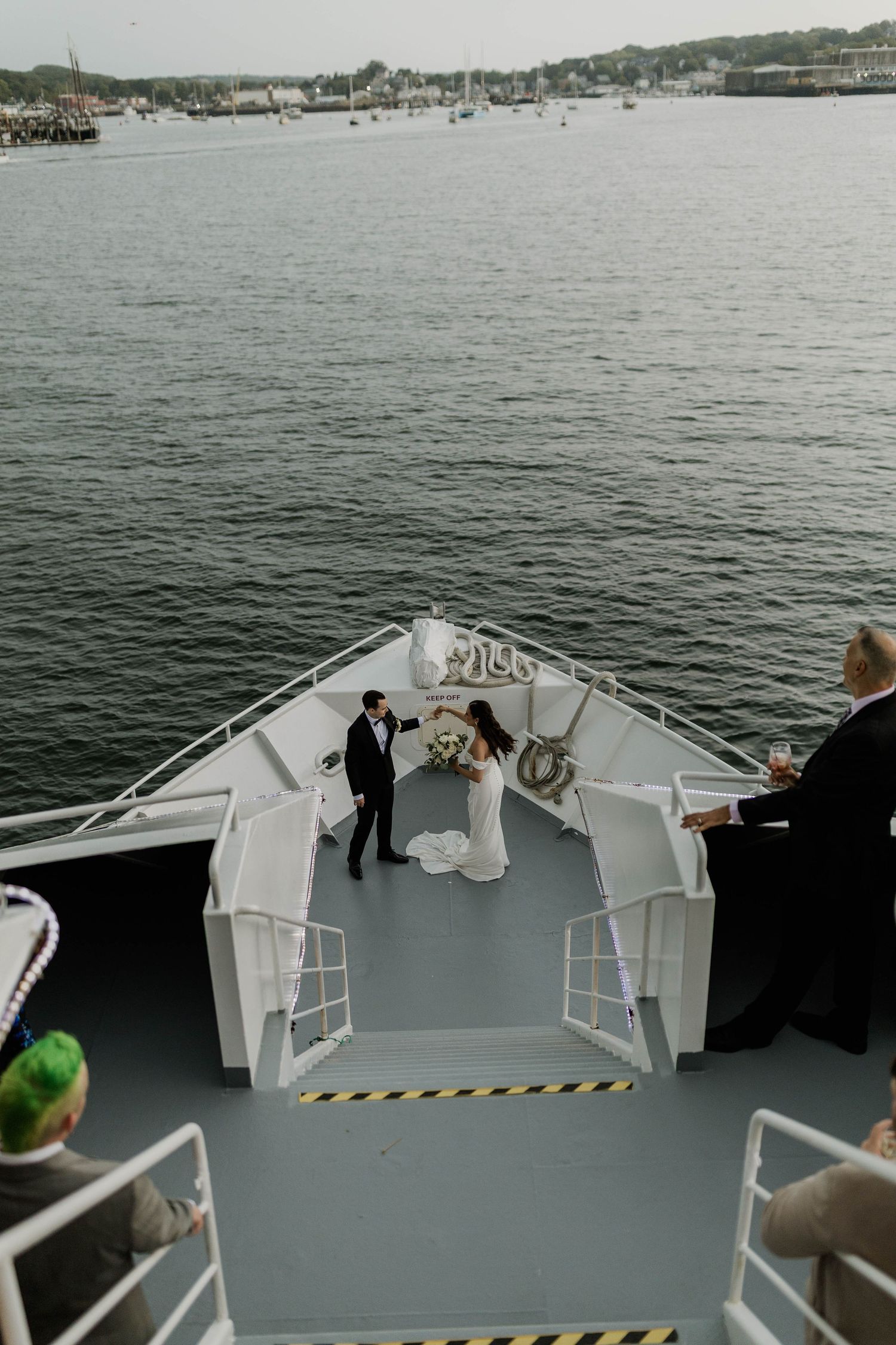 Aerial view of bride and groom toasting on bow of yacht on open water.