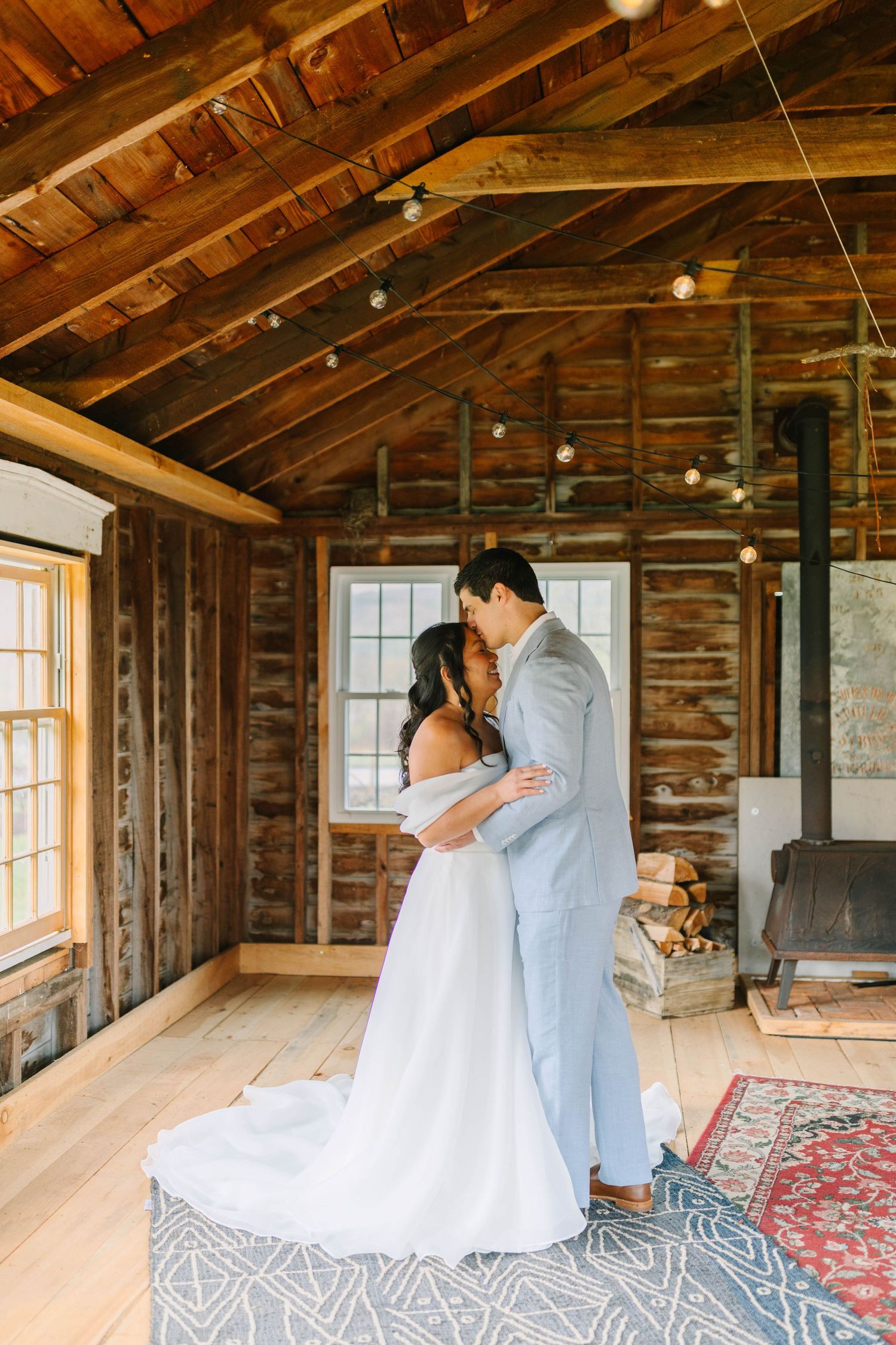 Bride and groom share intimate first look embrace in rustic log cabin with string lights.