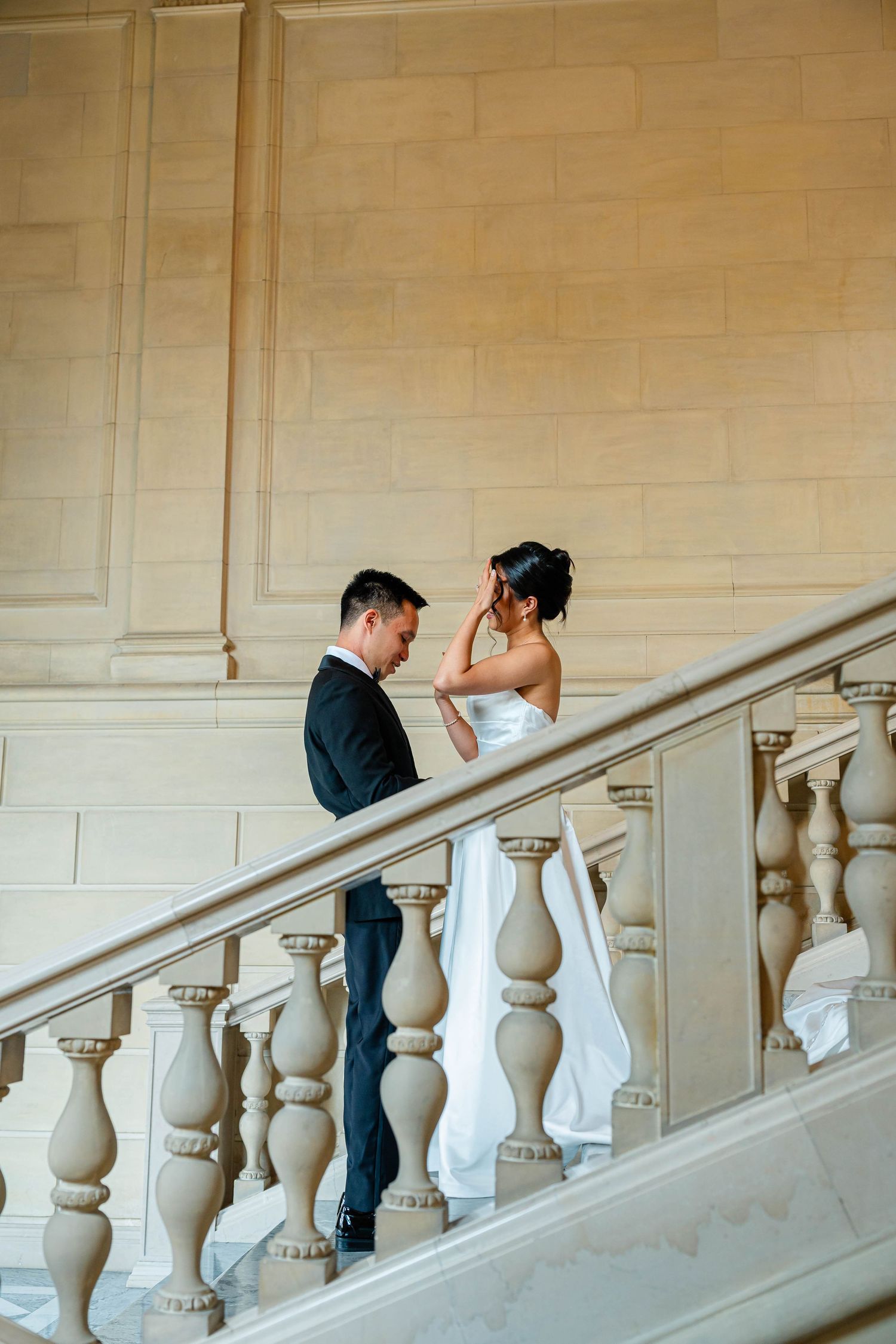 Bride and groom share tender moment on grand marble staircase in elegant venue.