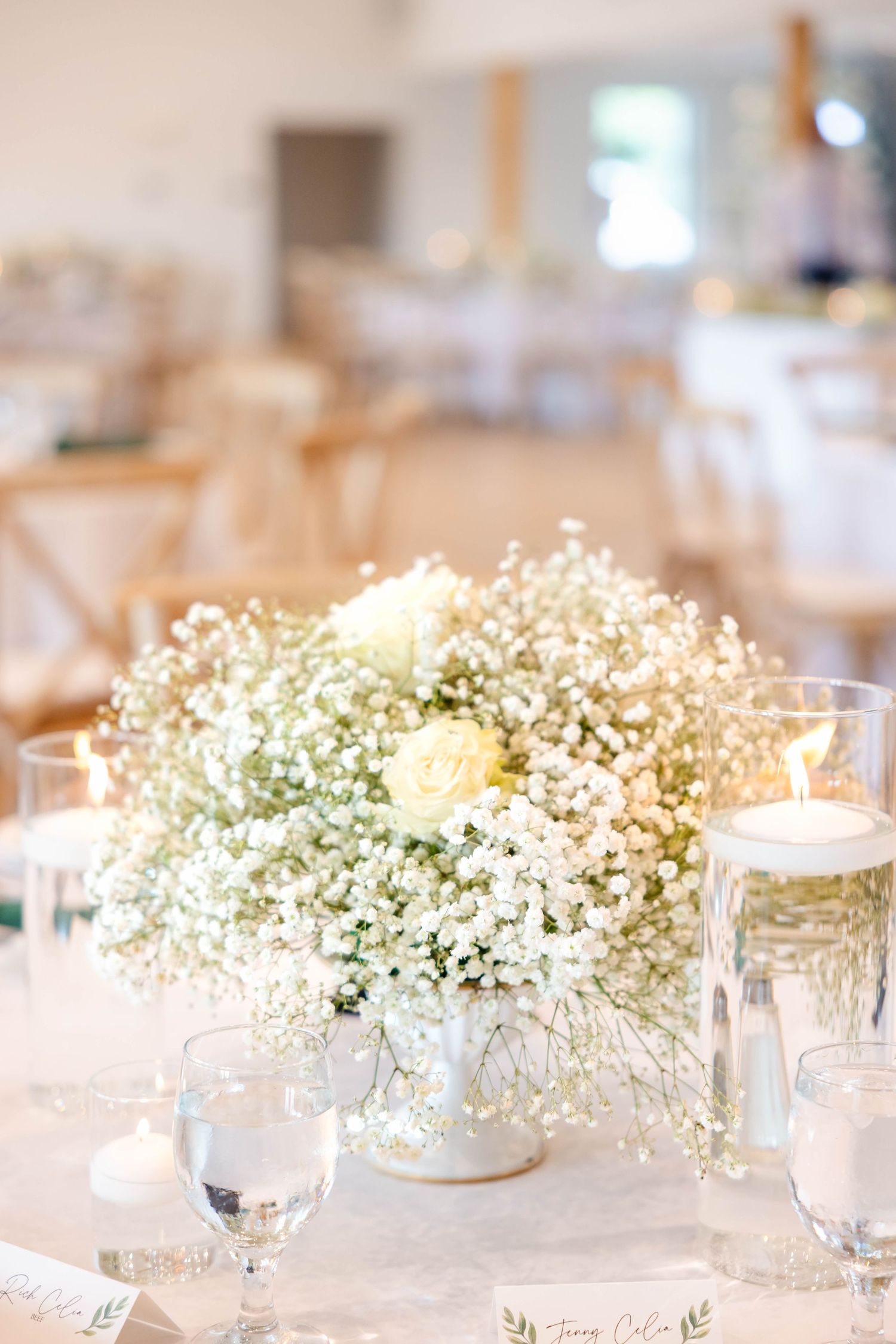 Baby's breath and white rose centerpiece with floating candles on a wedding reception table.