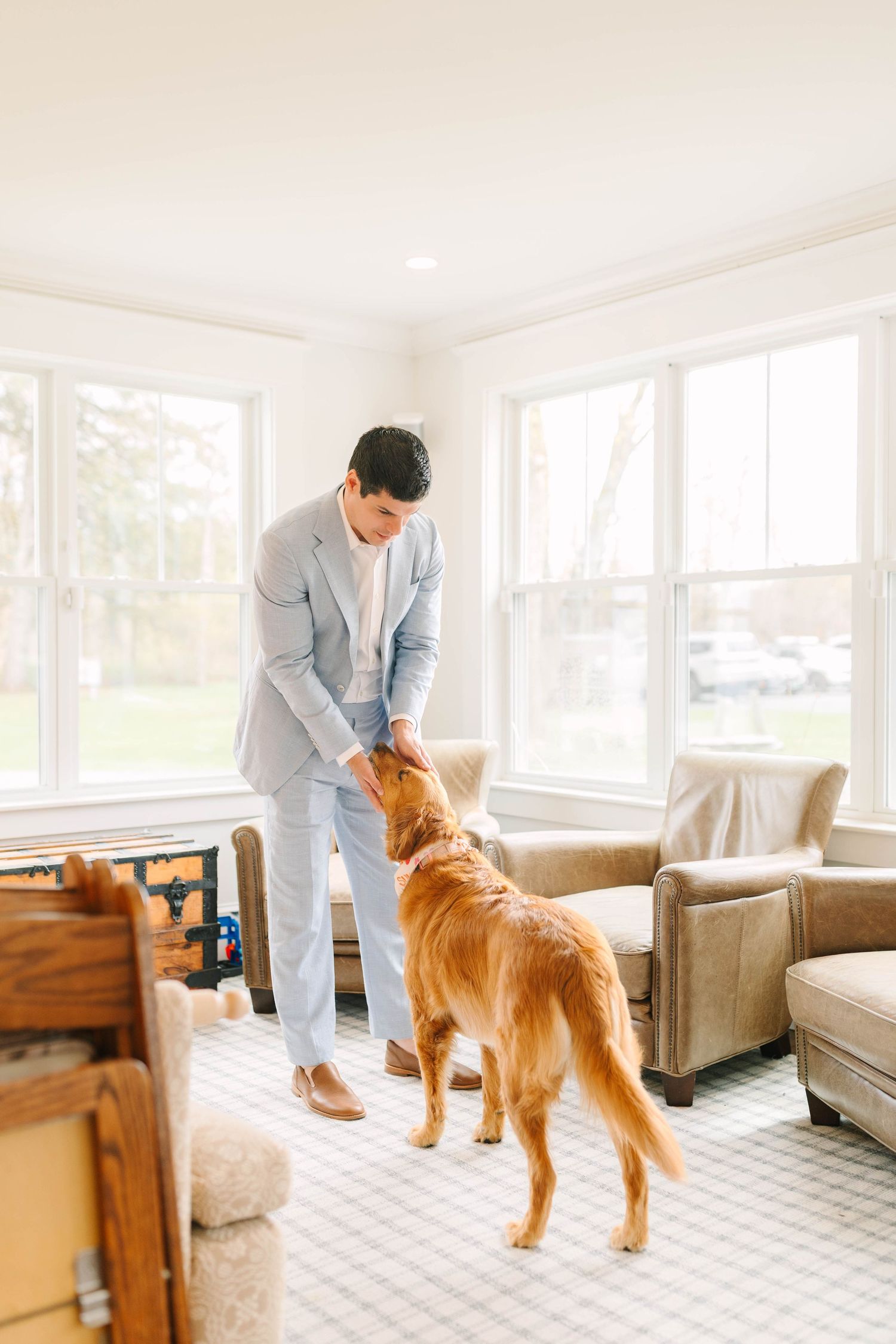 Man in light blue suit interacting with a golden retriever dog in an elegant sunroom.