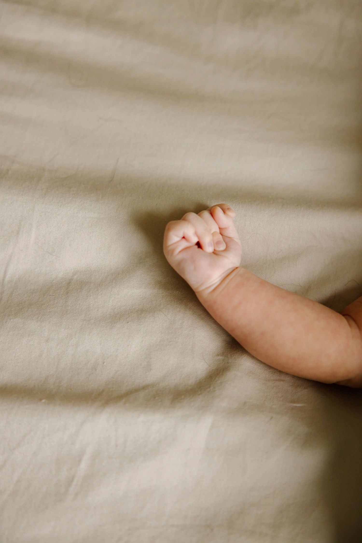 Close-up of a newborn baby's tiny clenched fist resting on a soft beige linen fabric.