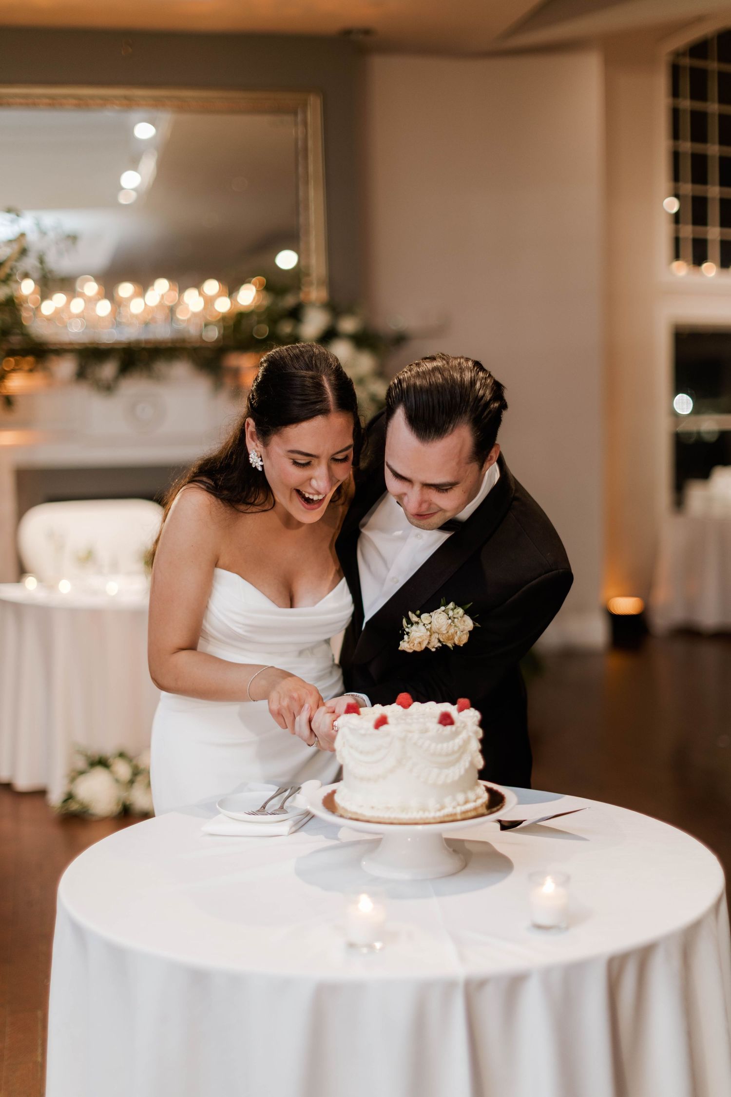 Bride and groom cutting white wedding cake decorated with fresh strawberries at reception.