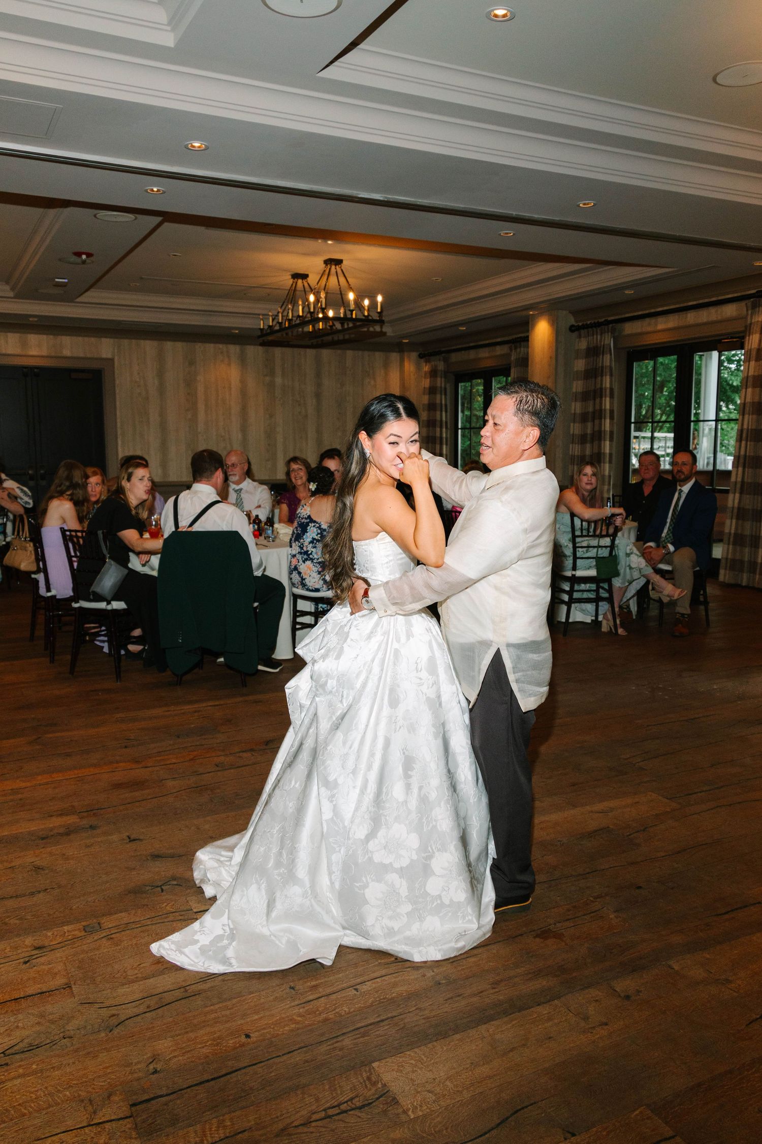 Emotional bride wipes tears during father-daughter dance at wedding reception.