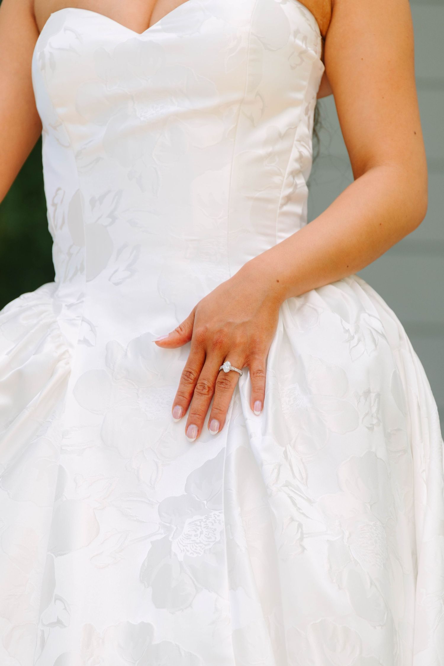Close-up of bride in white floral ballgown showcasing diamond engagement ring on her hand.