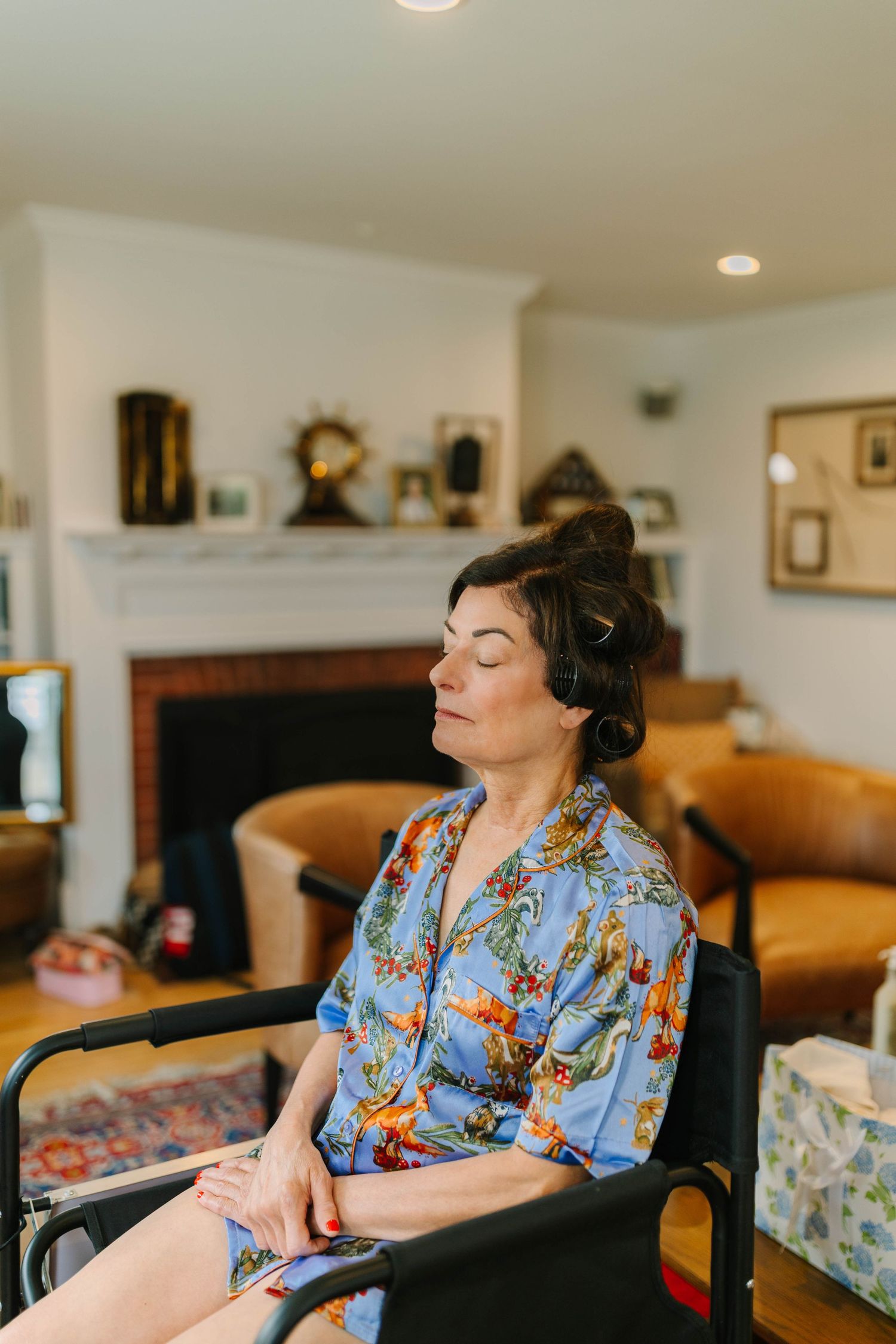 Woman in floral blue robe sits with eyes closed getting hair styled before wedding.
