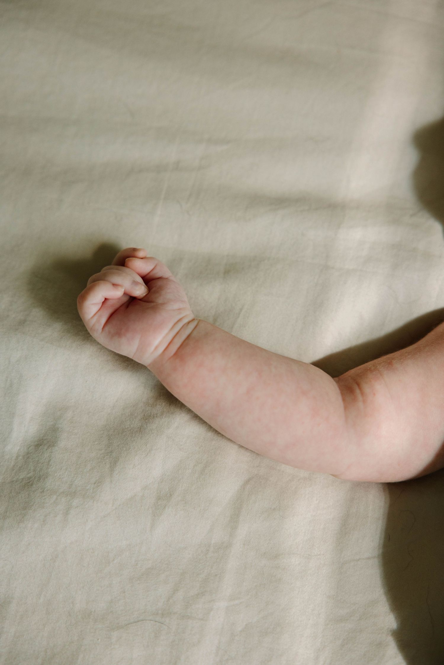 Close-up of a newborn baby's tiny hand and arm resting on a soft sage green linen fabric.
