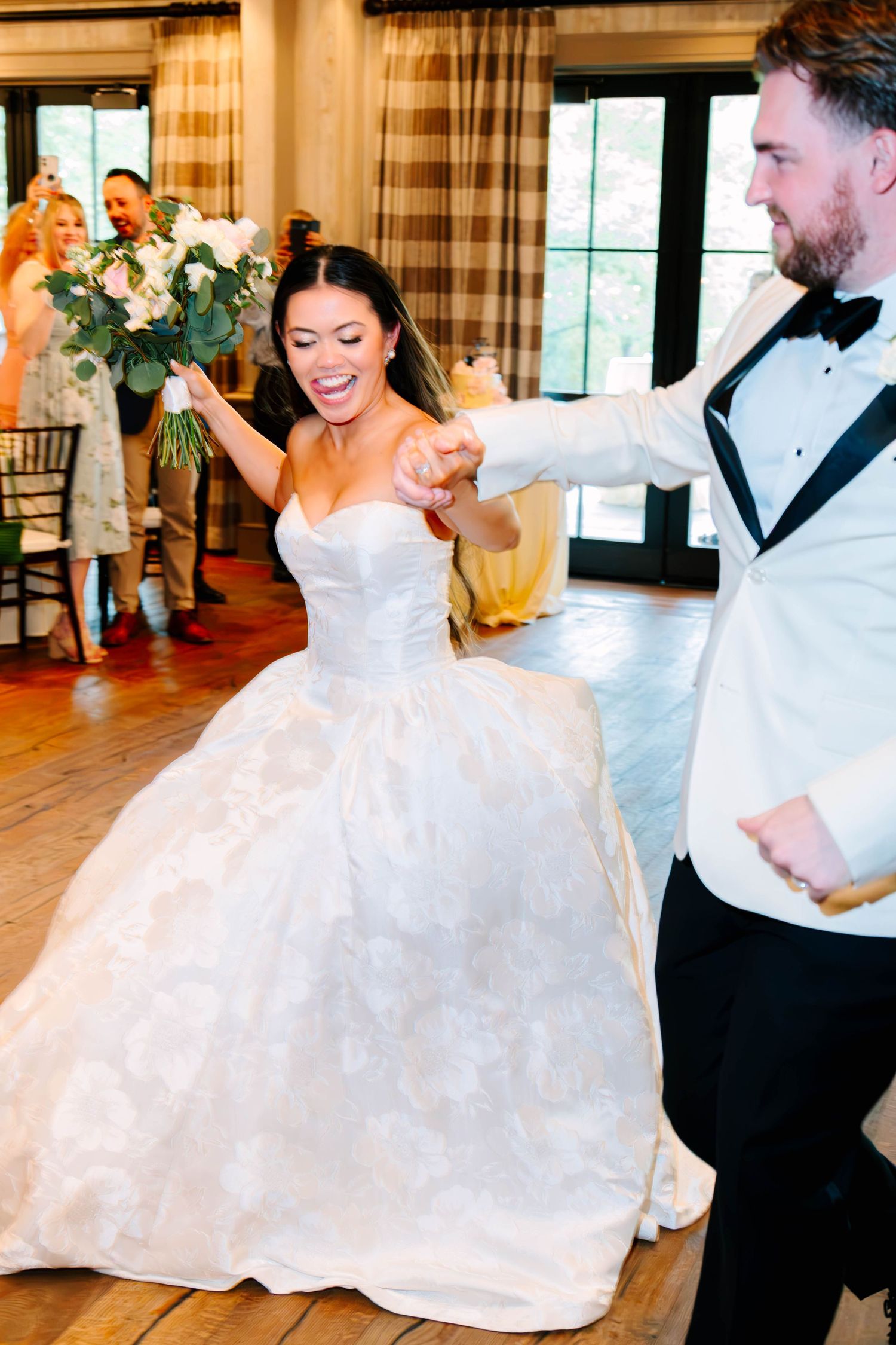 Joyful bride in white ballgown holds bouquet while dancing with groom at wedding reception.