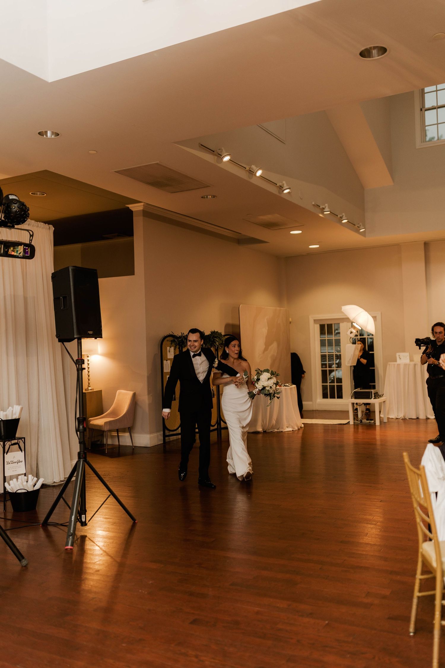 Bride in white gown and groom in tuxedo make grand entrance into elegant wedding reception venue.