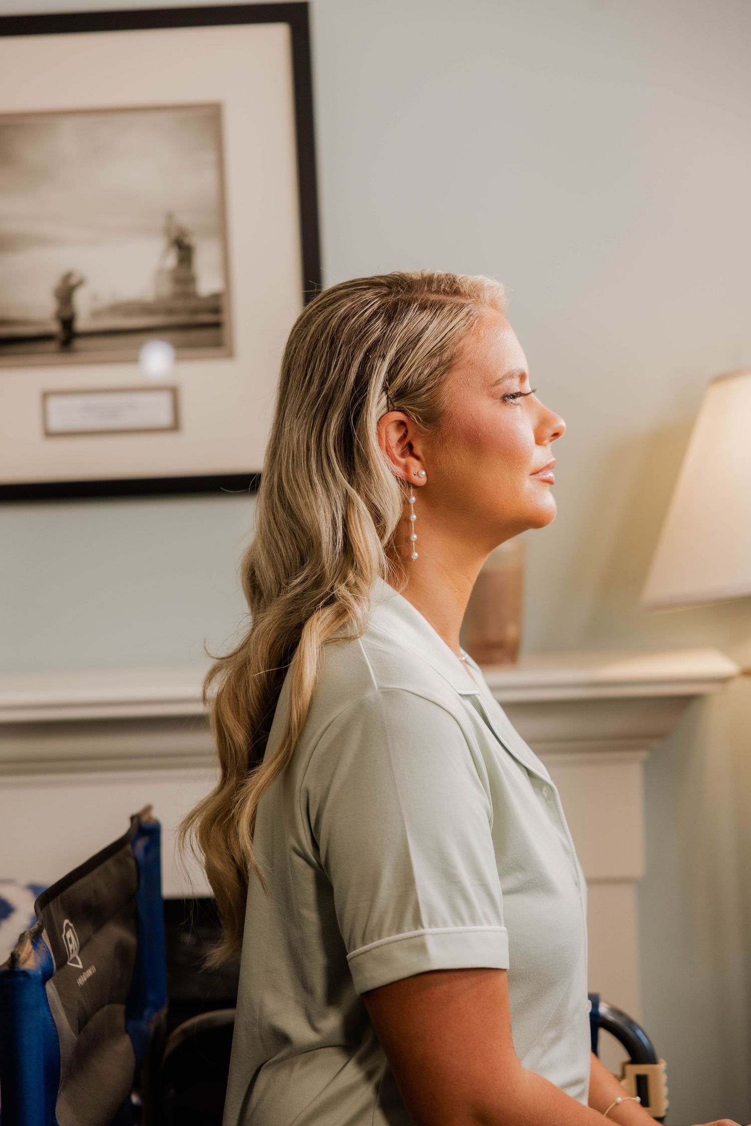 Blonde bridesmaid in sage green dress with pearl earrings and elegant wavy hairstyle.