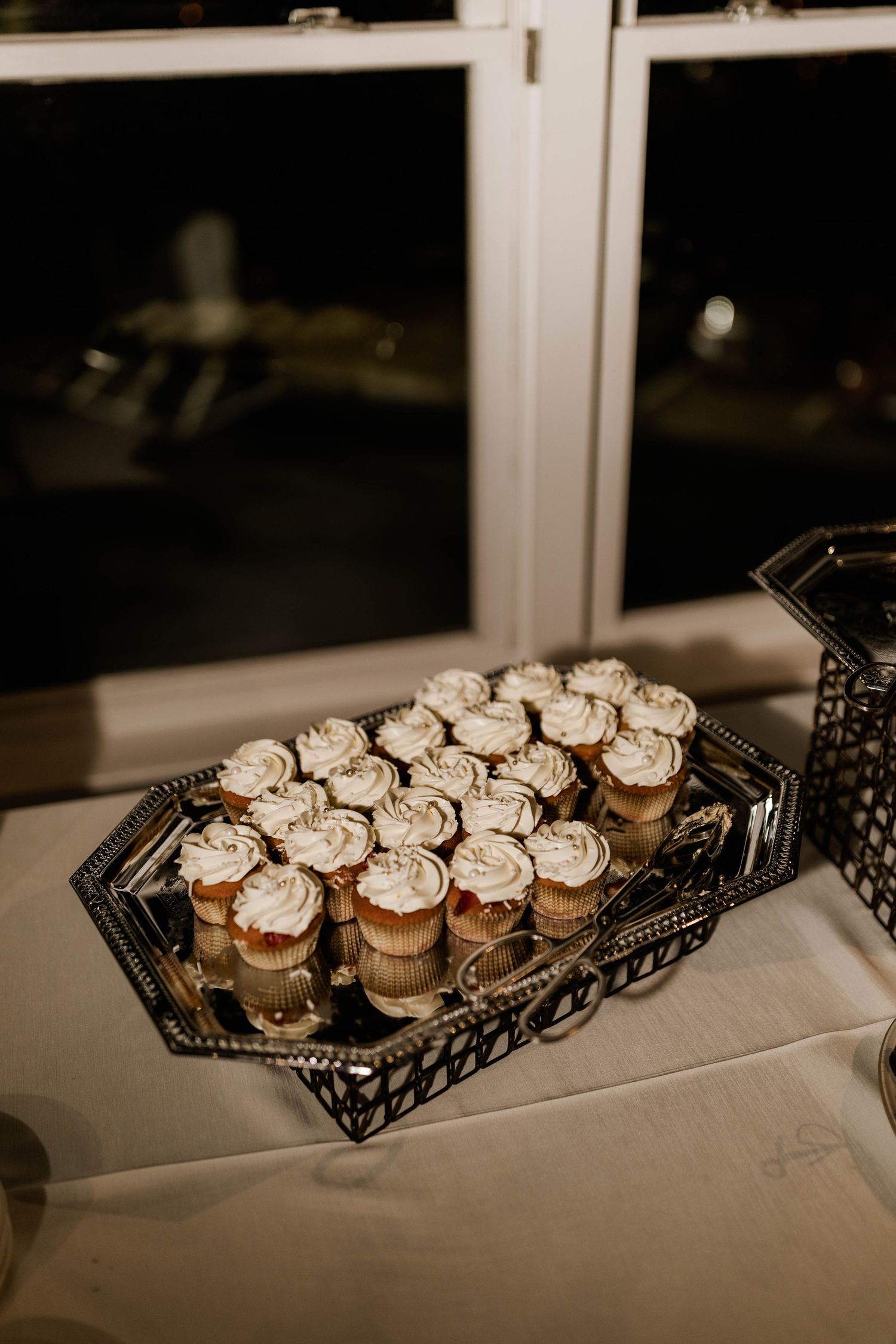Silver tray of white frosted cupcakes displayed on table at elegant wedding dessert station.