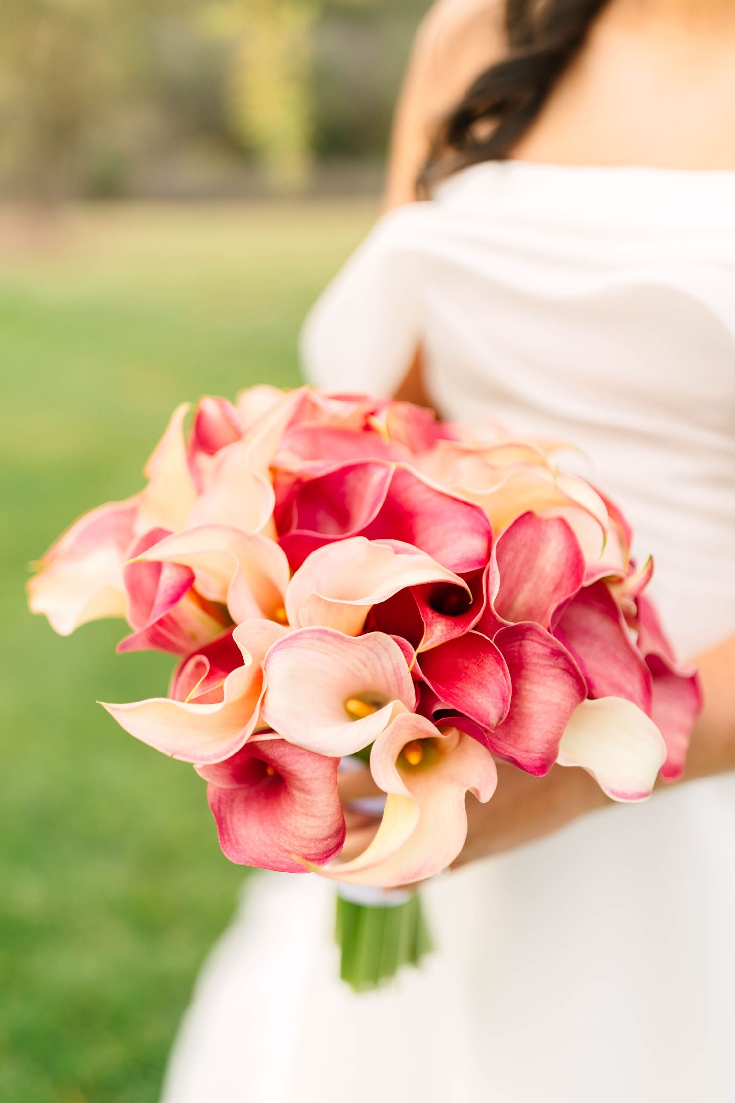 Bride holding a lush bouquet of pink and cream calla lilies at an outdoor wedding ceremony.