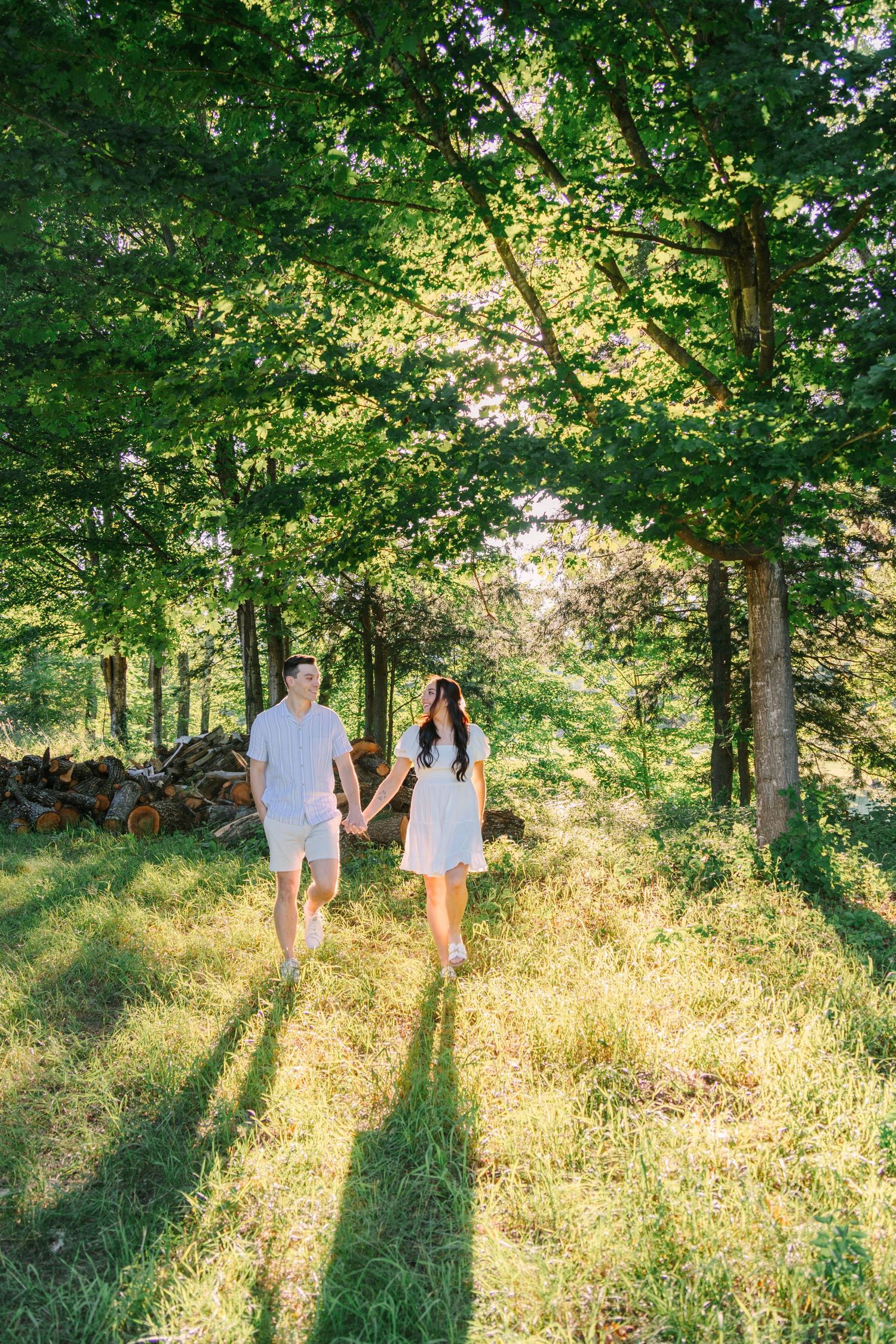 Couple holding hands walking through a sunlit green forest path on a sunny day.