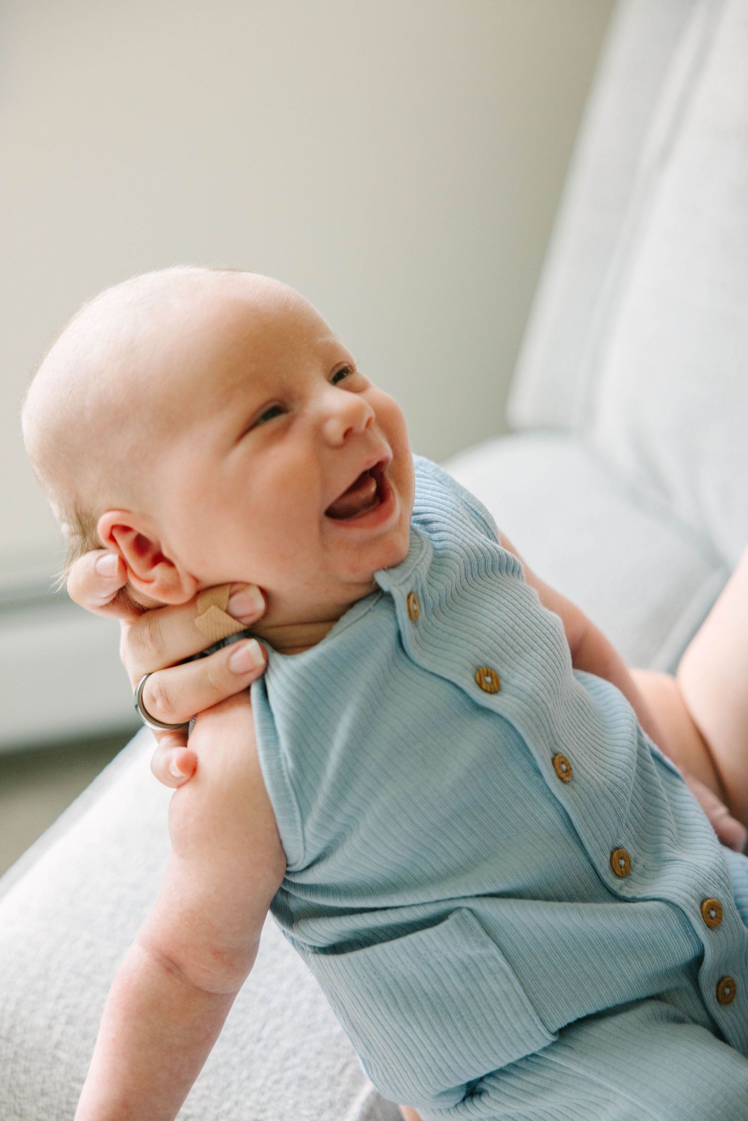 Smiling baby in a light blue ribbed romper being held up by an adult's hands.