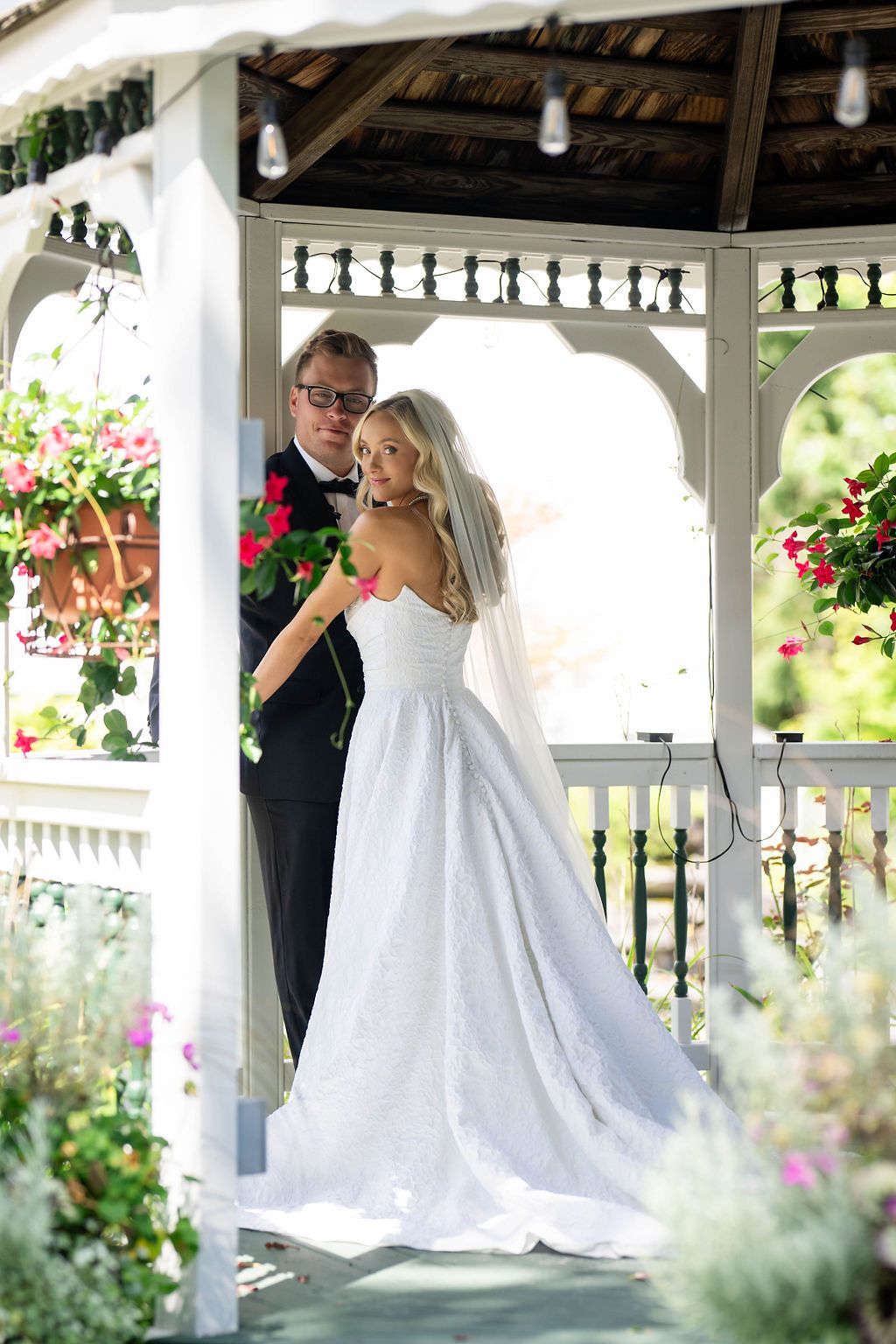 Bride and groom share a romantic moment in a white gazebo adorned with colorful flowers on their wedding day.