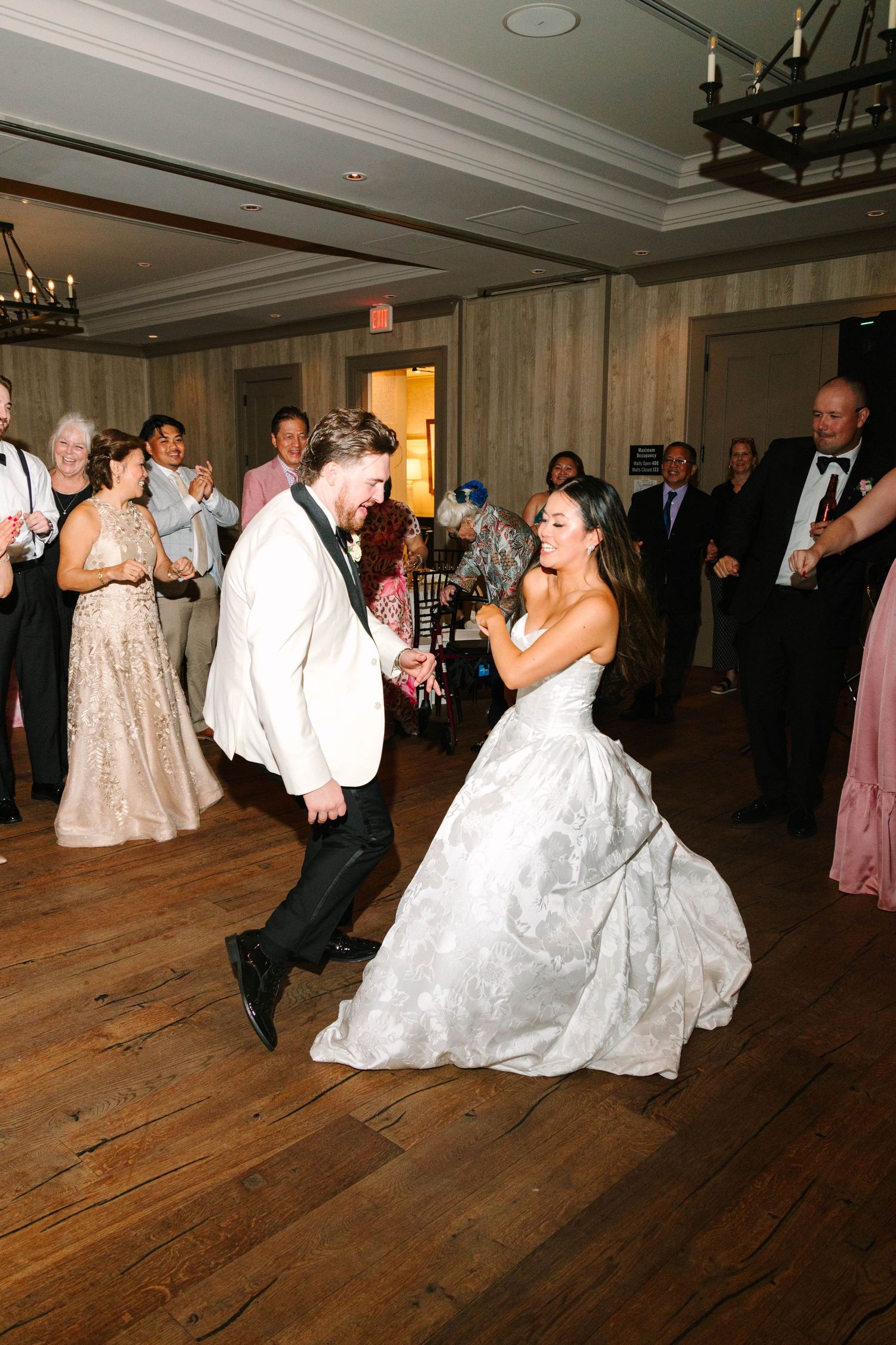 Bride and groom dance energetically together surrounded by cheering guests at reception.