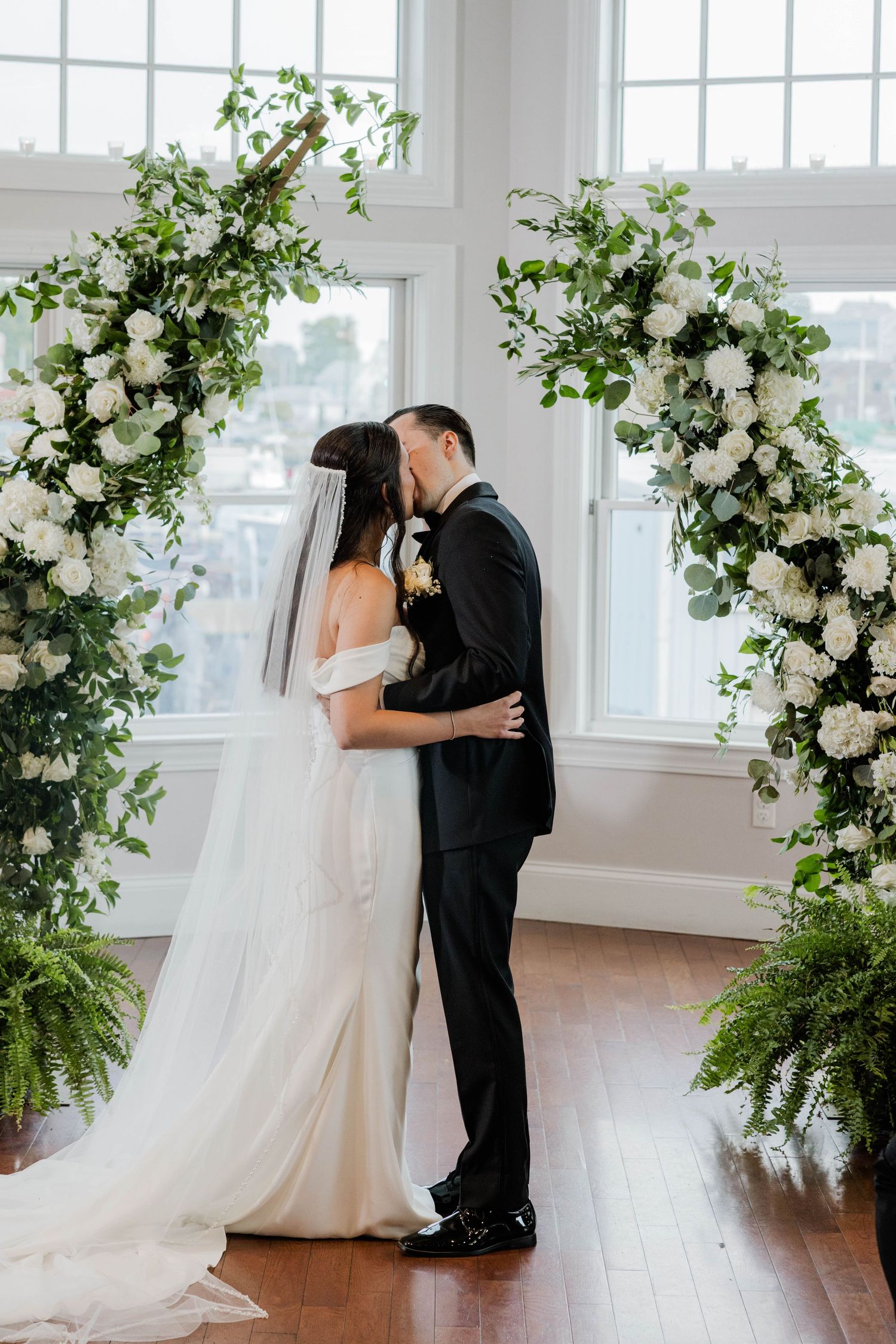 Bride and groom sharing first kiss under floral arch at wedding.
