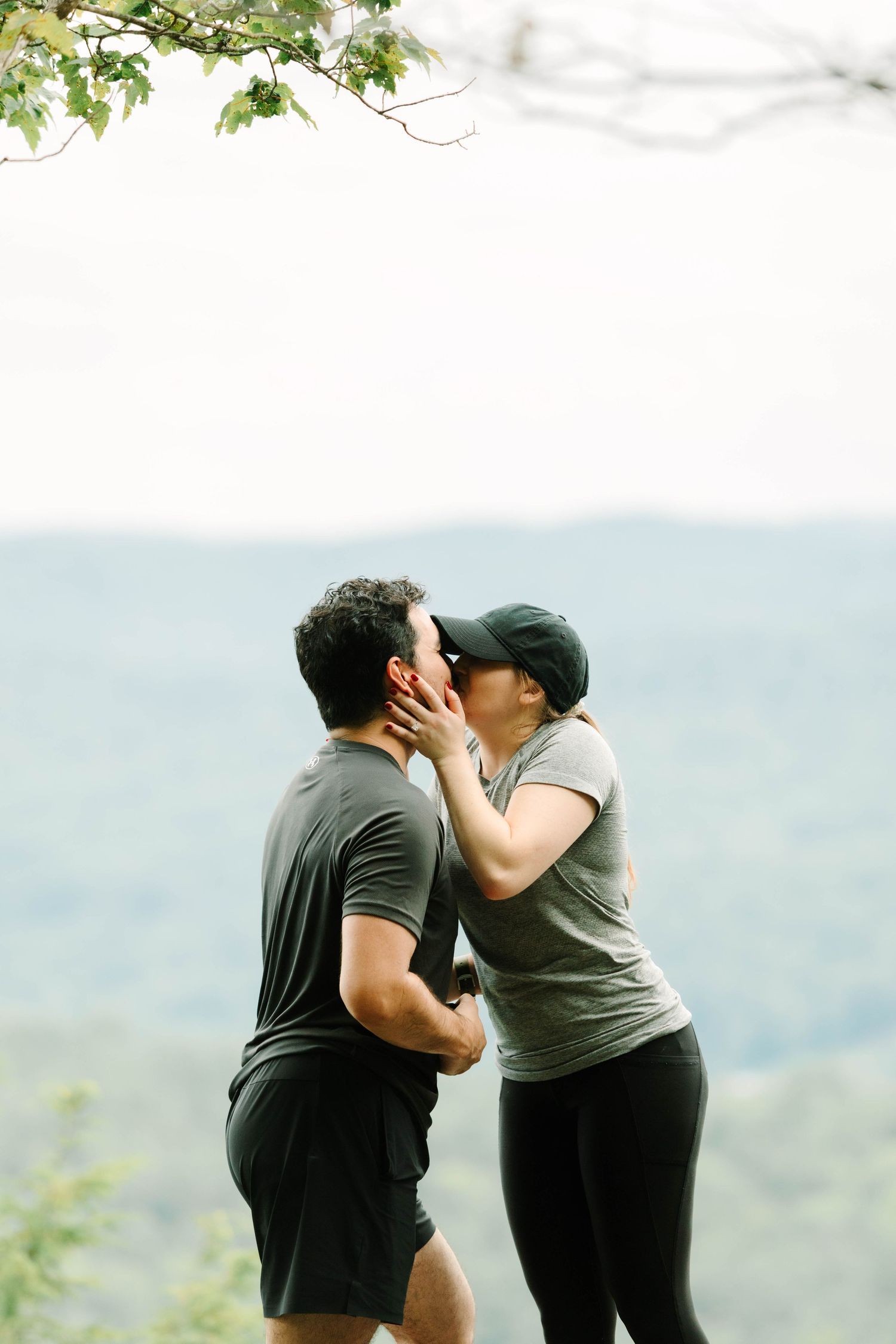 Couple sharing a passionate kiss on a scenic mountain overlook with rolling green hills in background.