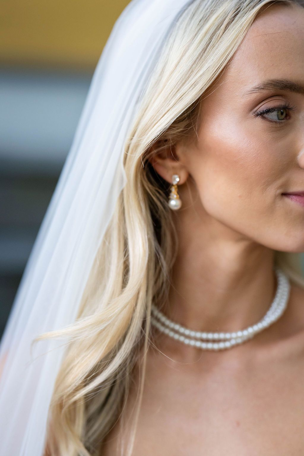 Close-up of bride wearing pearl drop earrings and double-strand pearl necklace with a white wedding veil.