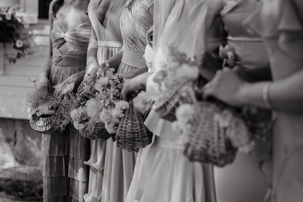 Black and white photo of bridesmaids holding floral bouquets and wicker baskets in flowing gowns.