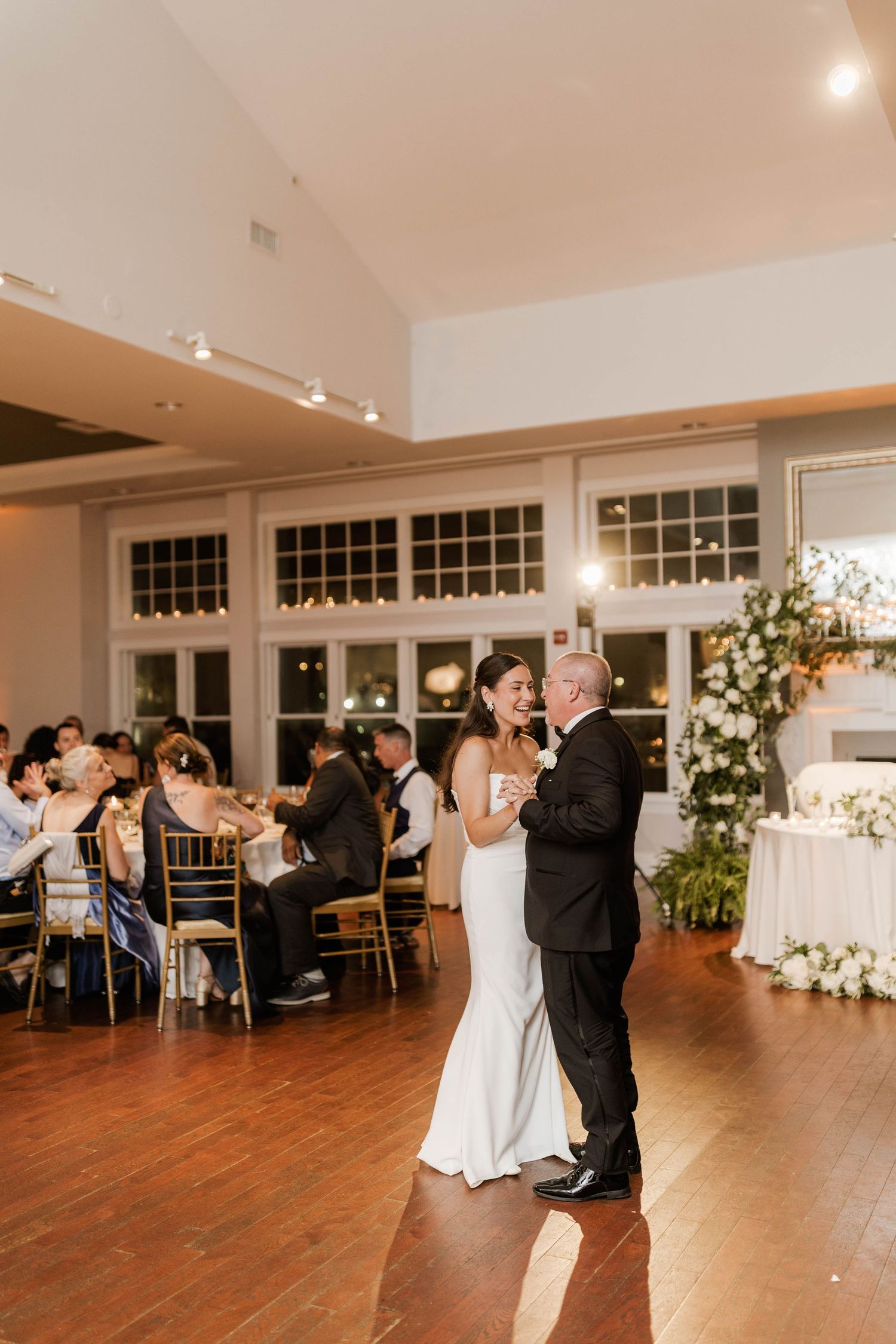 Bride and father share an emotional first dance at elegant wedding reception with gold chairs and floral arrangements.