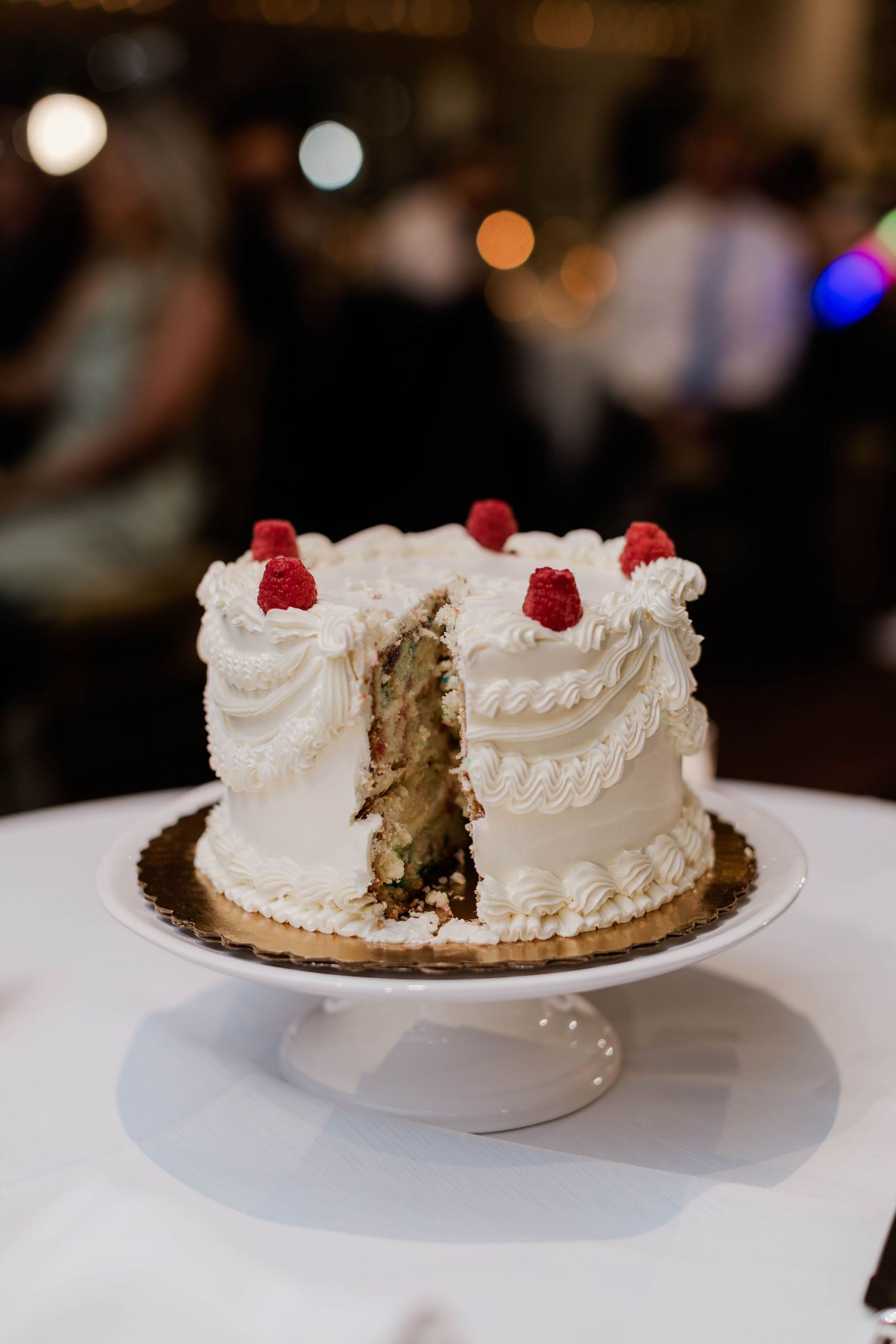 White wedding cake with raspberry topping and a slice removed on a cake stand.
