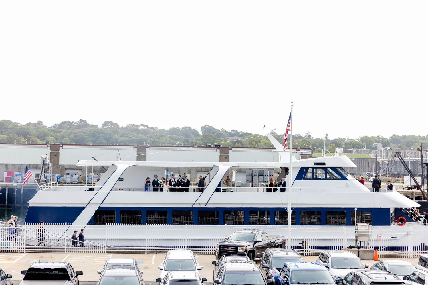 Wedding guests gathered on a large white yacht docked at a coastal marina on an overcast day.