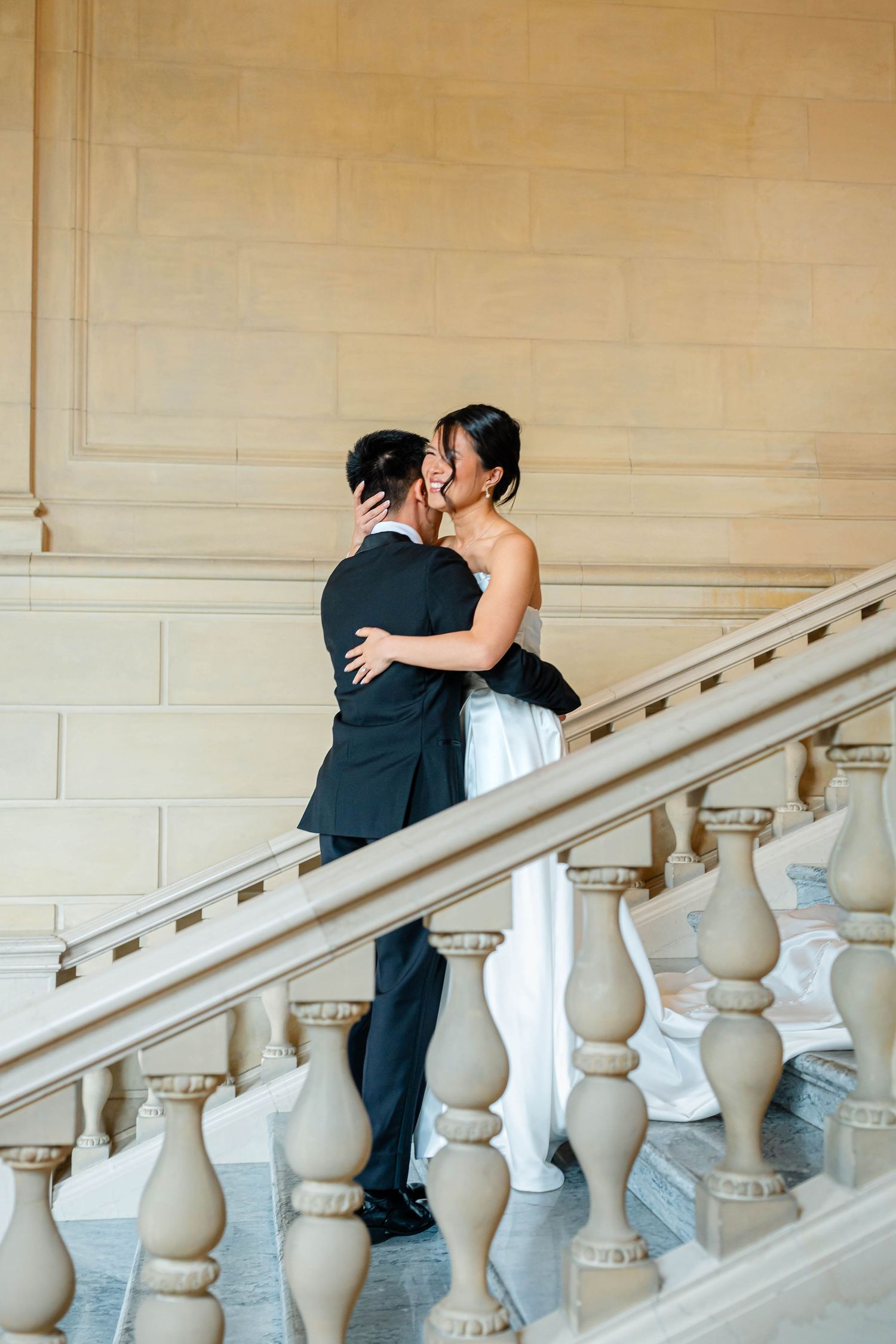 Bride and groom sharing a romantic kiss on grand marble staircase with ornate stone balustrade.