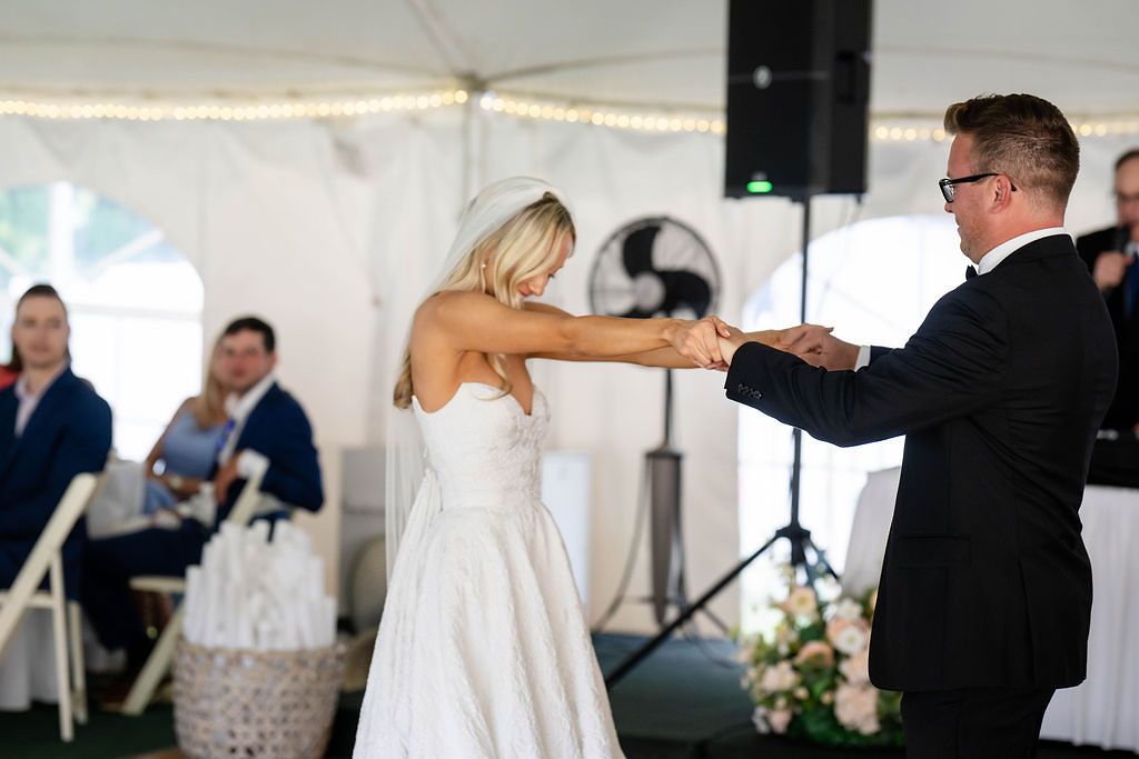 Bride and groom share their first dance under a white tent at elegant wedding reception.