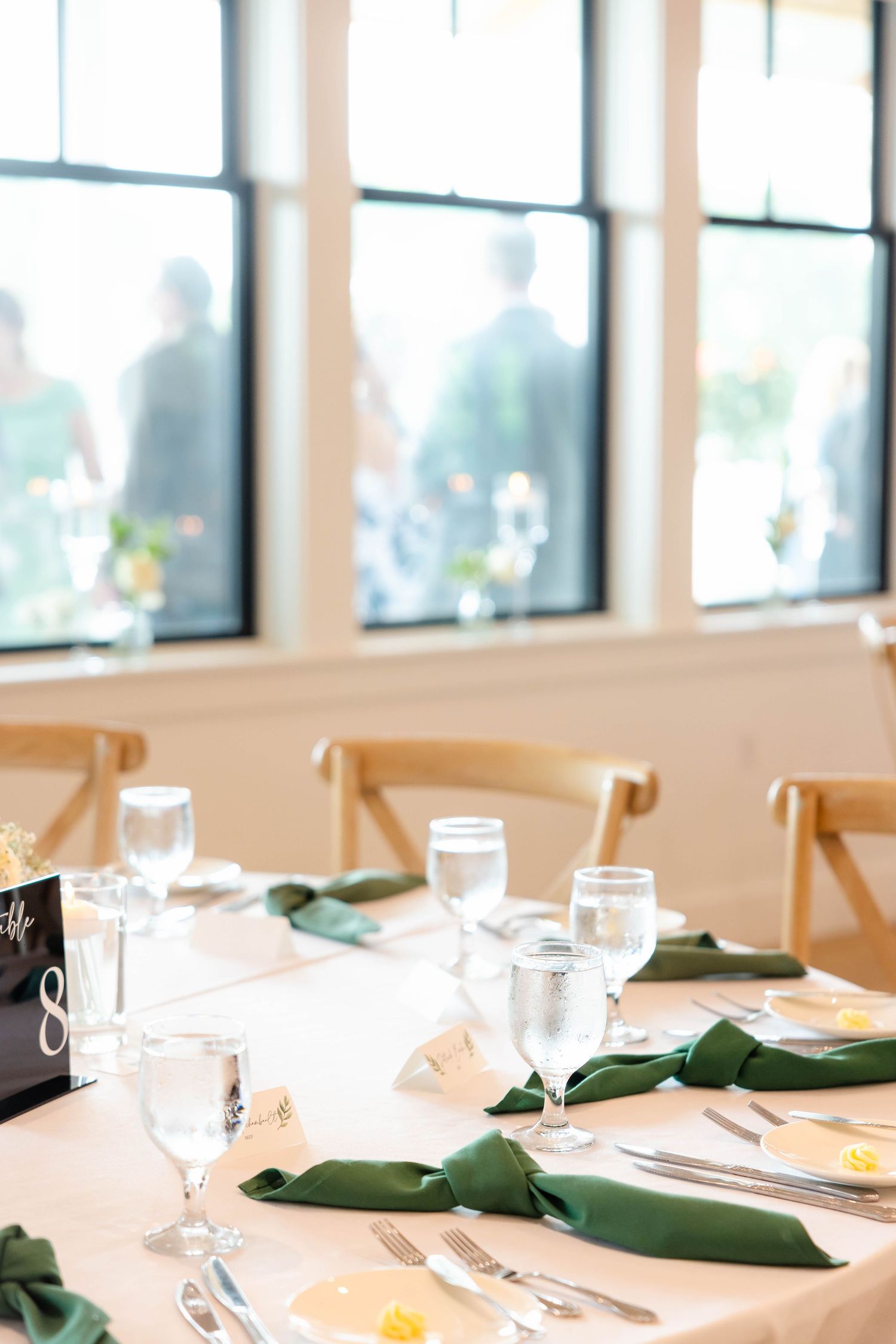 Elegant wedding reception table set with green napkins, crystal glassware, and table number eight card.